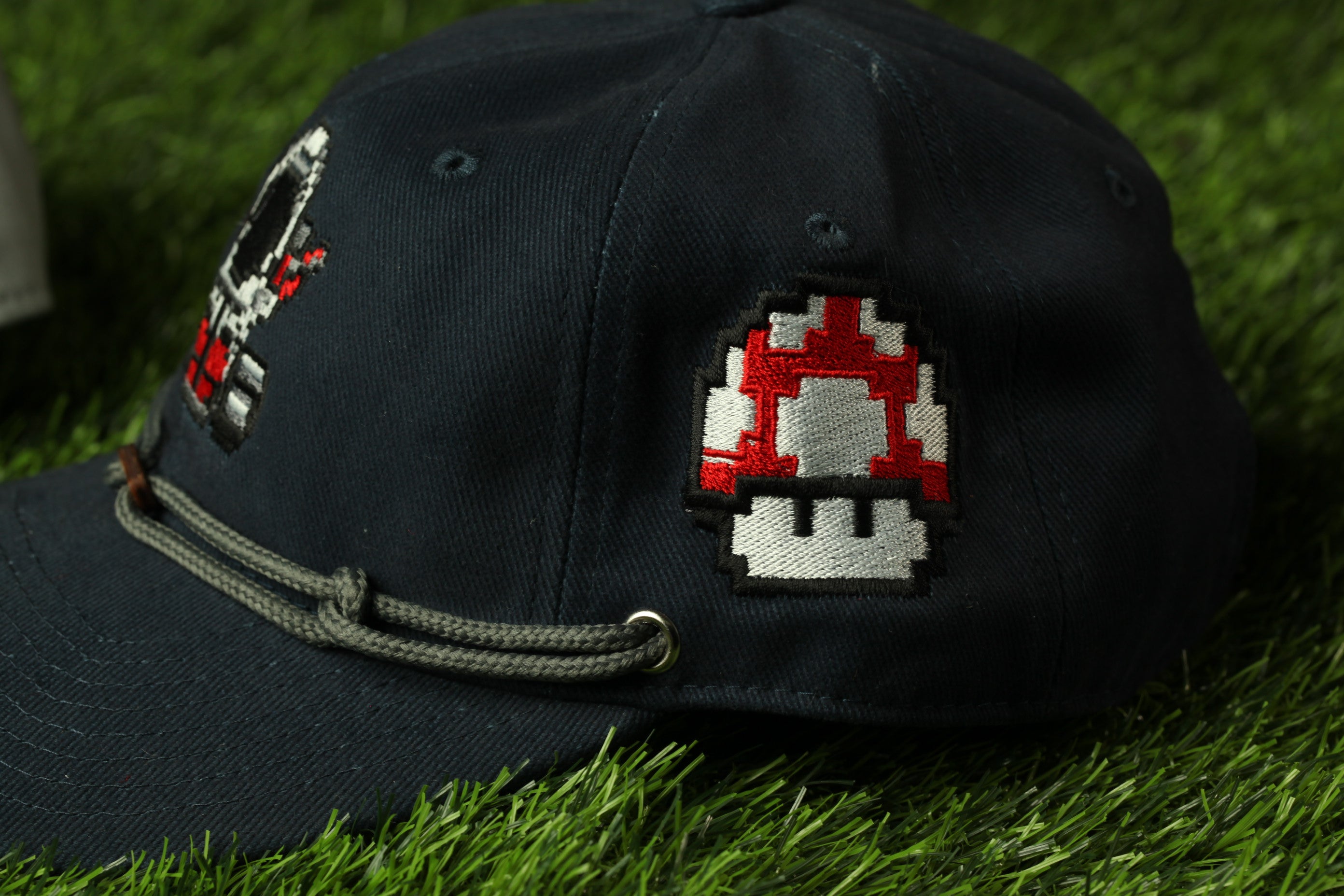 A black baseball cap with a mushroom-shaped patch on the side, lying on a grassy surface.