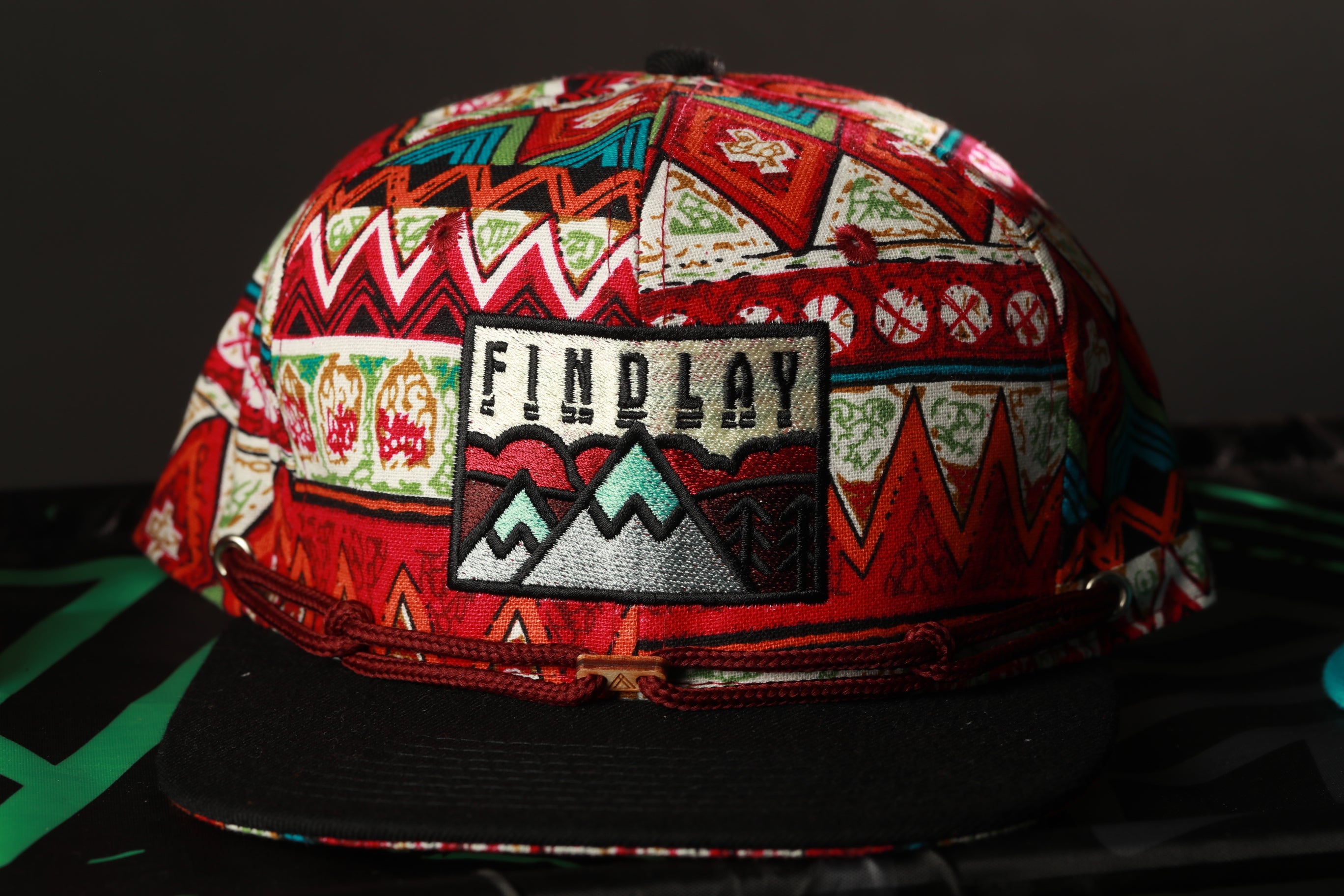 A colorful, patterned baseball cap with a mountain design and the word "FINDlay" printed on it.