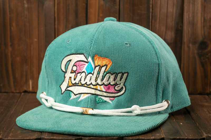 A turquoise baseball cap with a white strap and a colorful embroidered logo on the front, placed on a wooden surface.