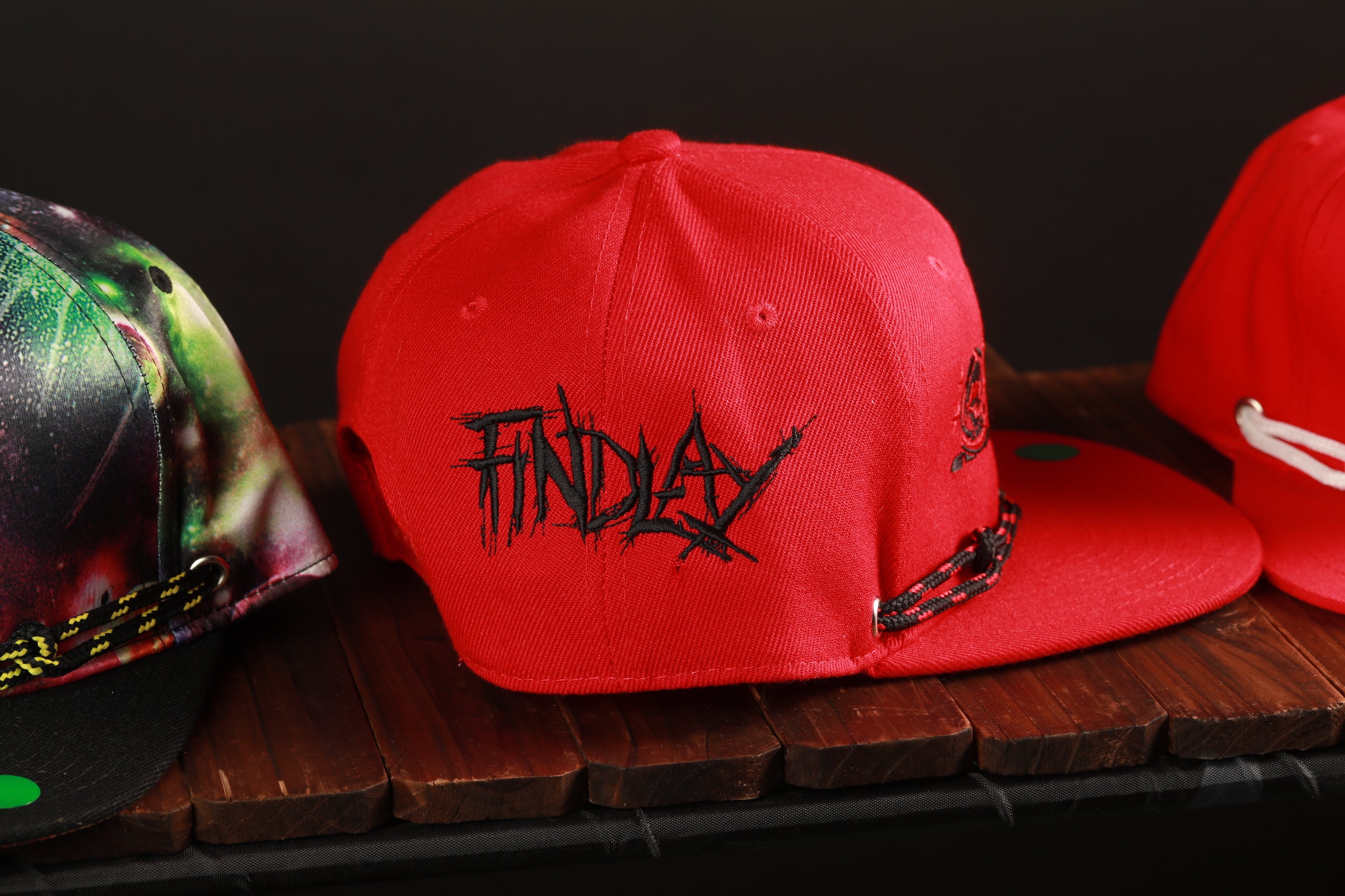 A red baseball cap with the word "FINDAY" printed on it, sitting on a wooden surface.
