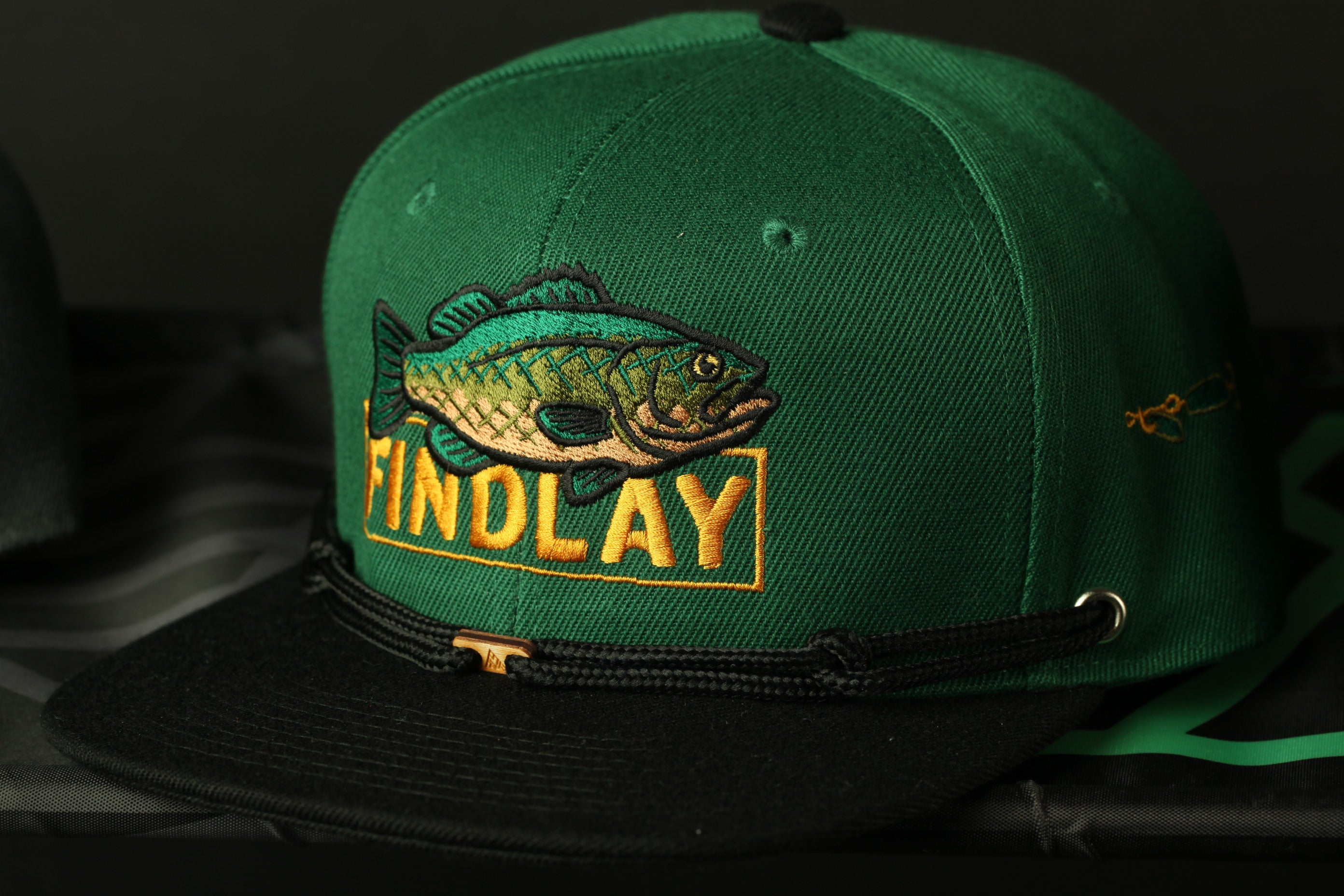 A green baseball cap with a fish embroidered on it, featuring the word "FINDLAY" in yellow text.