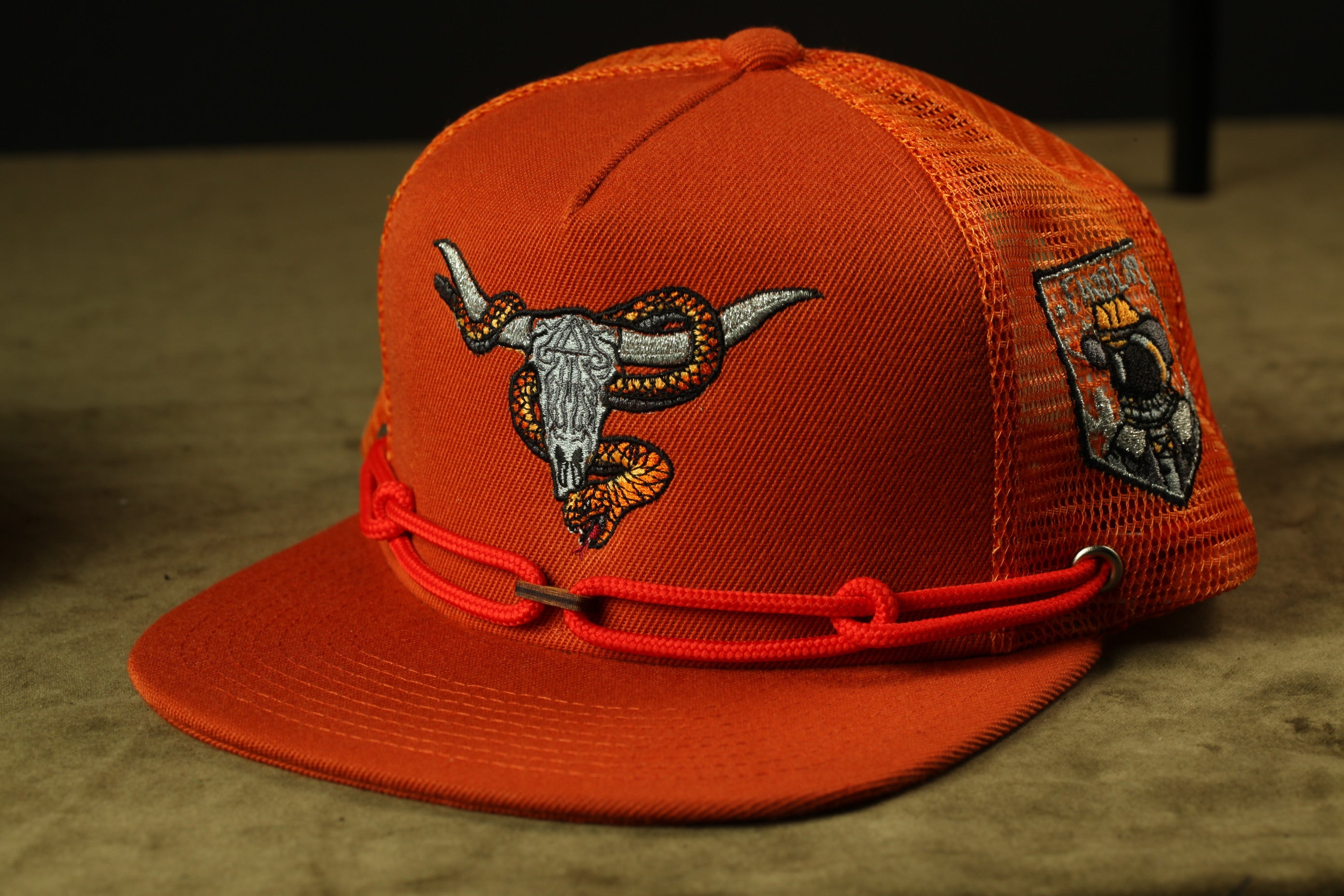 An orange baseball cap with a red string and a graphic of a bull's head on the front.