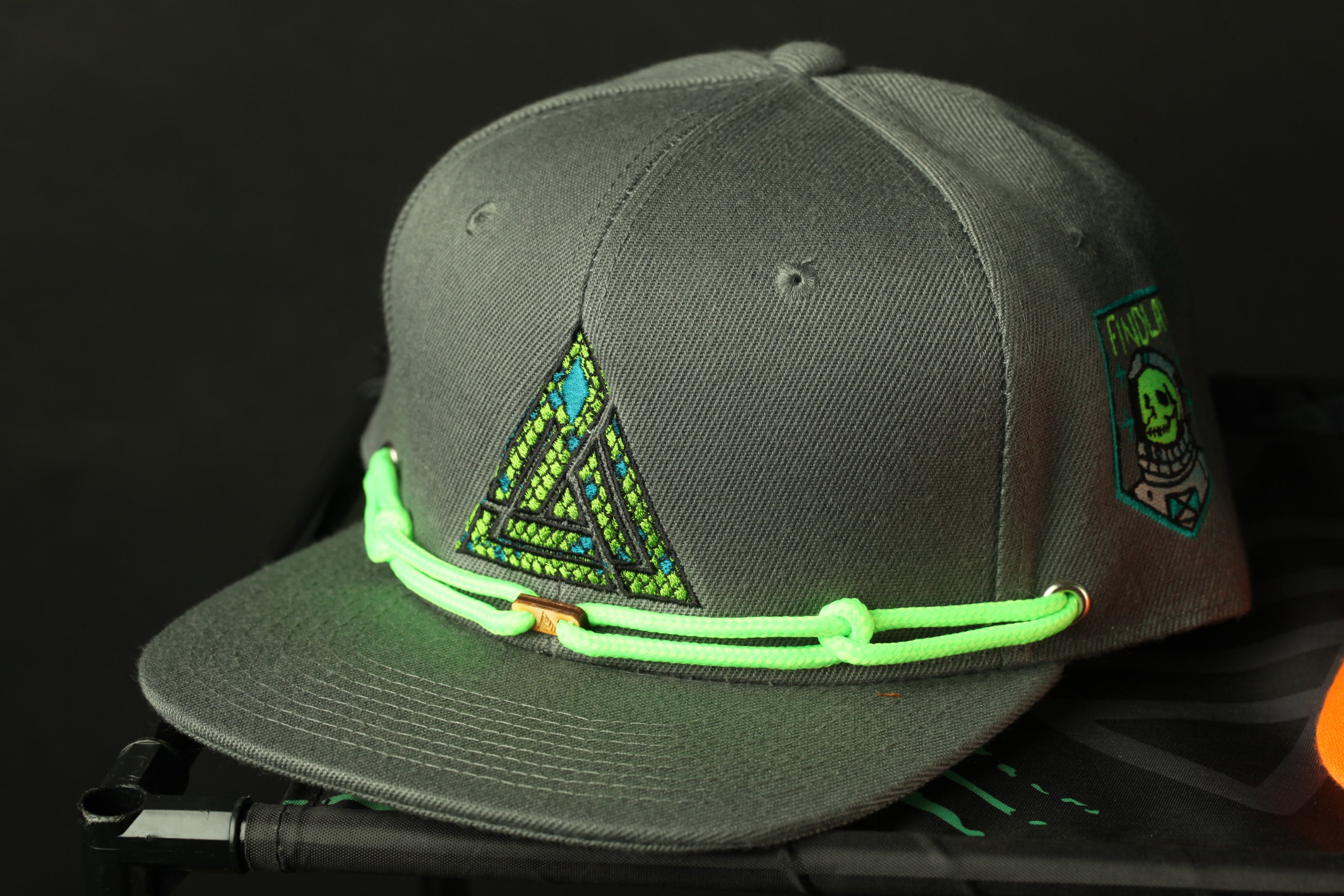 A gray baseball cap with a neon green string and a triangle design on the front.