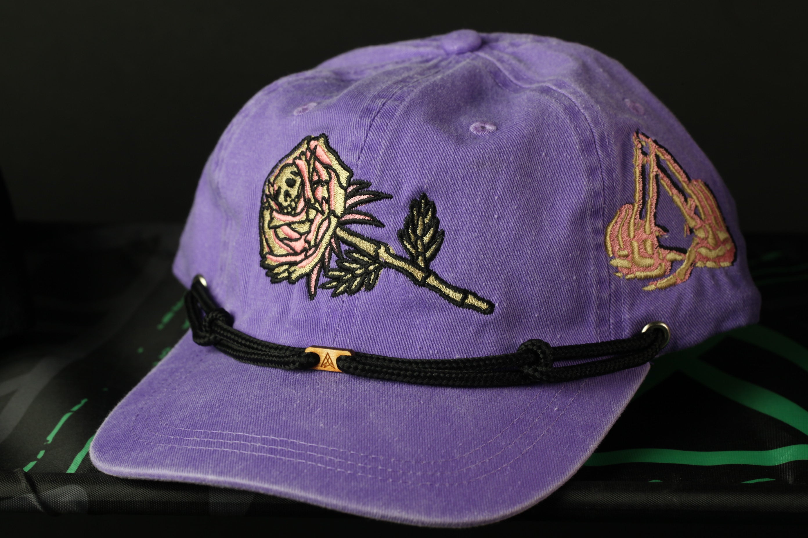 A purple baseball cap with a rose embroidered on it, sitting on a black surface.