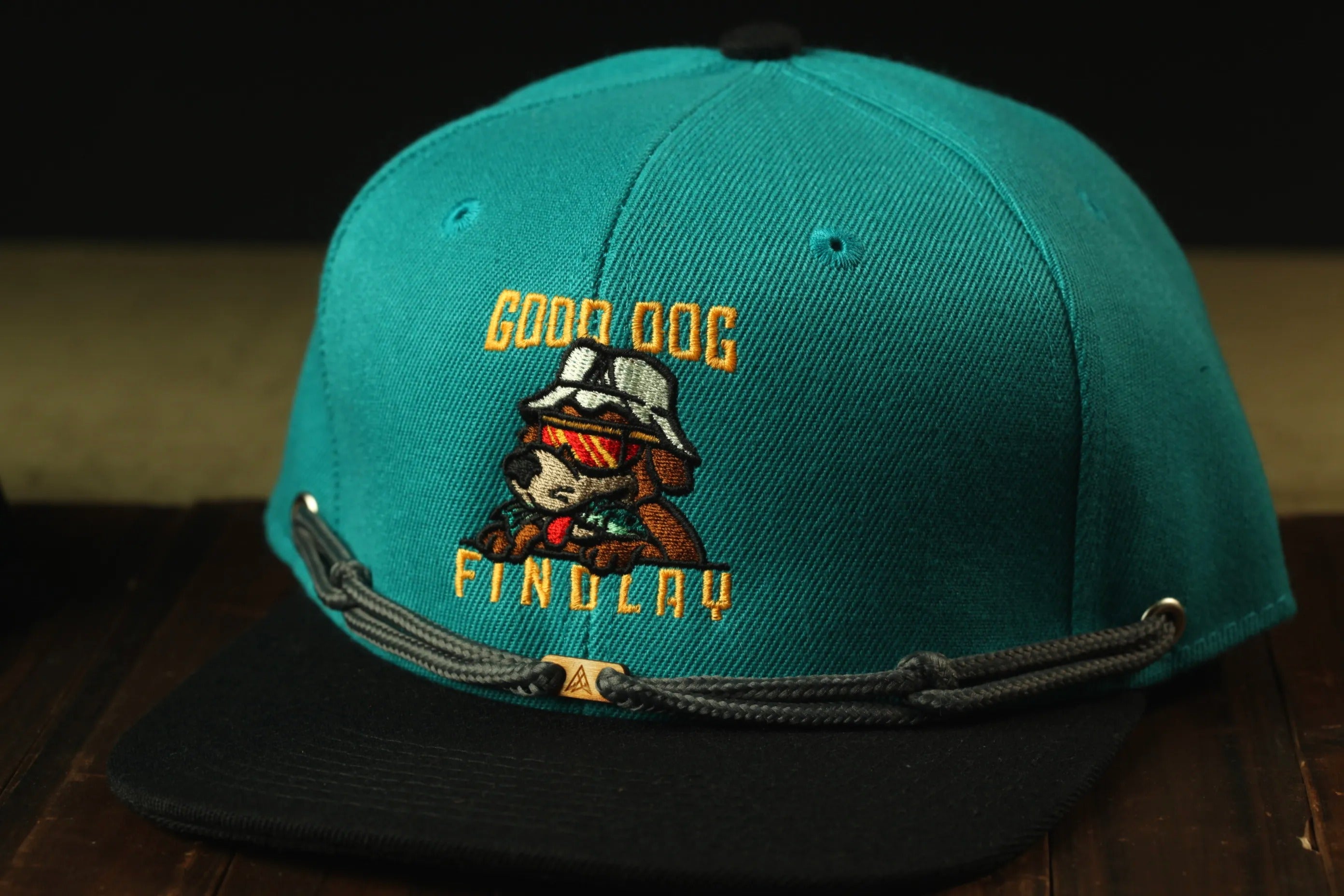 A turquoise baseball cap with a graphic of a dog and the text "GOOD DOG FIND LAY" printed on it.