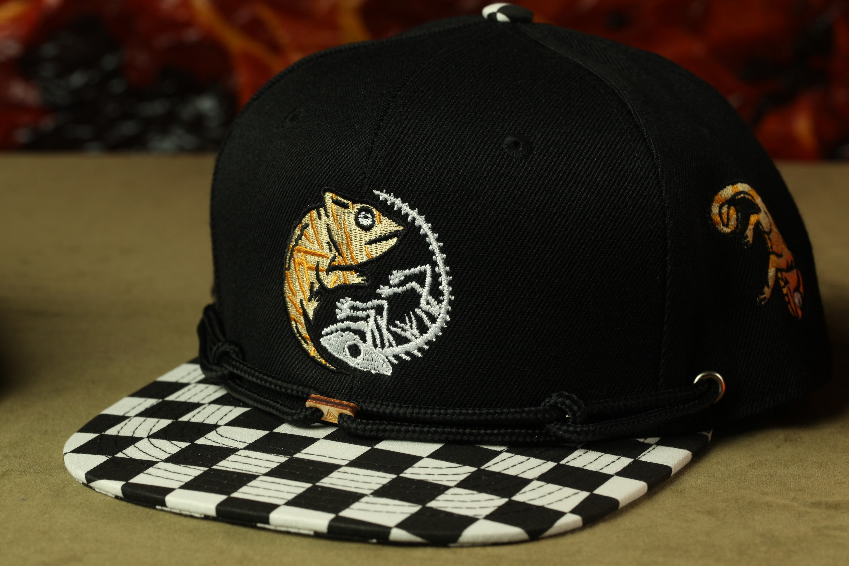 A black baseball cap with a checkered pattern and a chameleon design on the front.