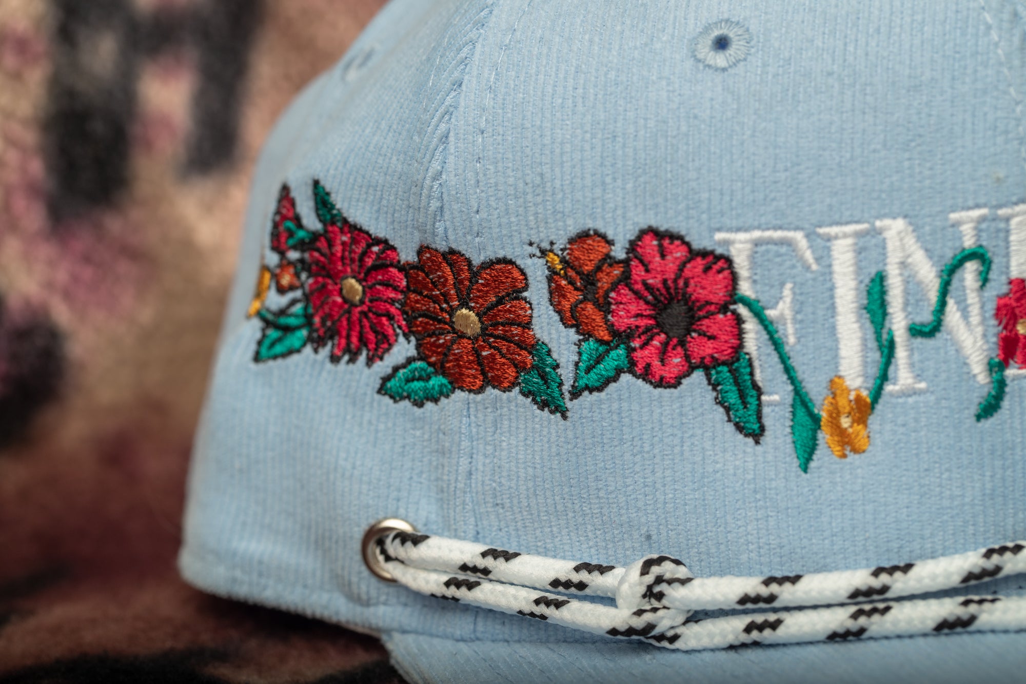 A close-up view of a light blue baseball cap with colorful floral embroidery.