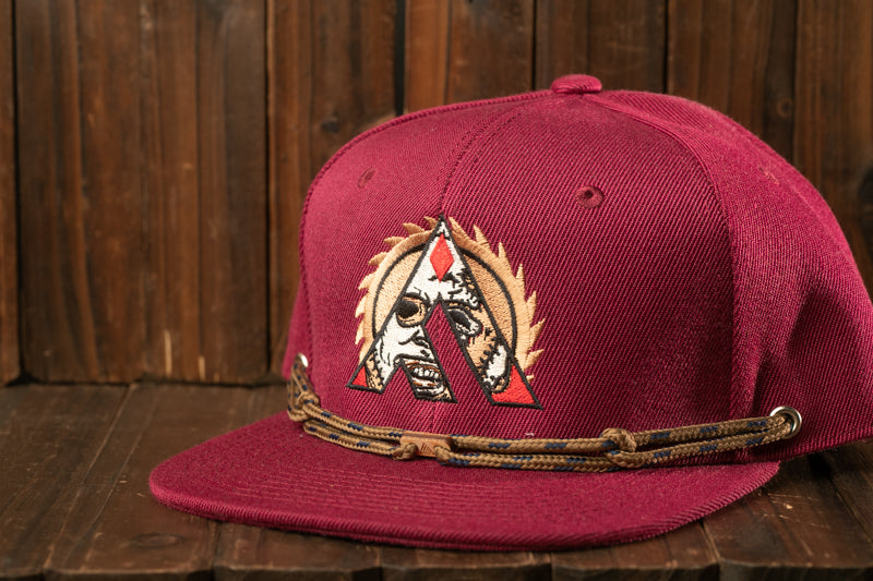 A maroon baseball cap with a distinctive logo is displayed on a wooden surface.