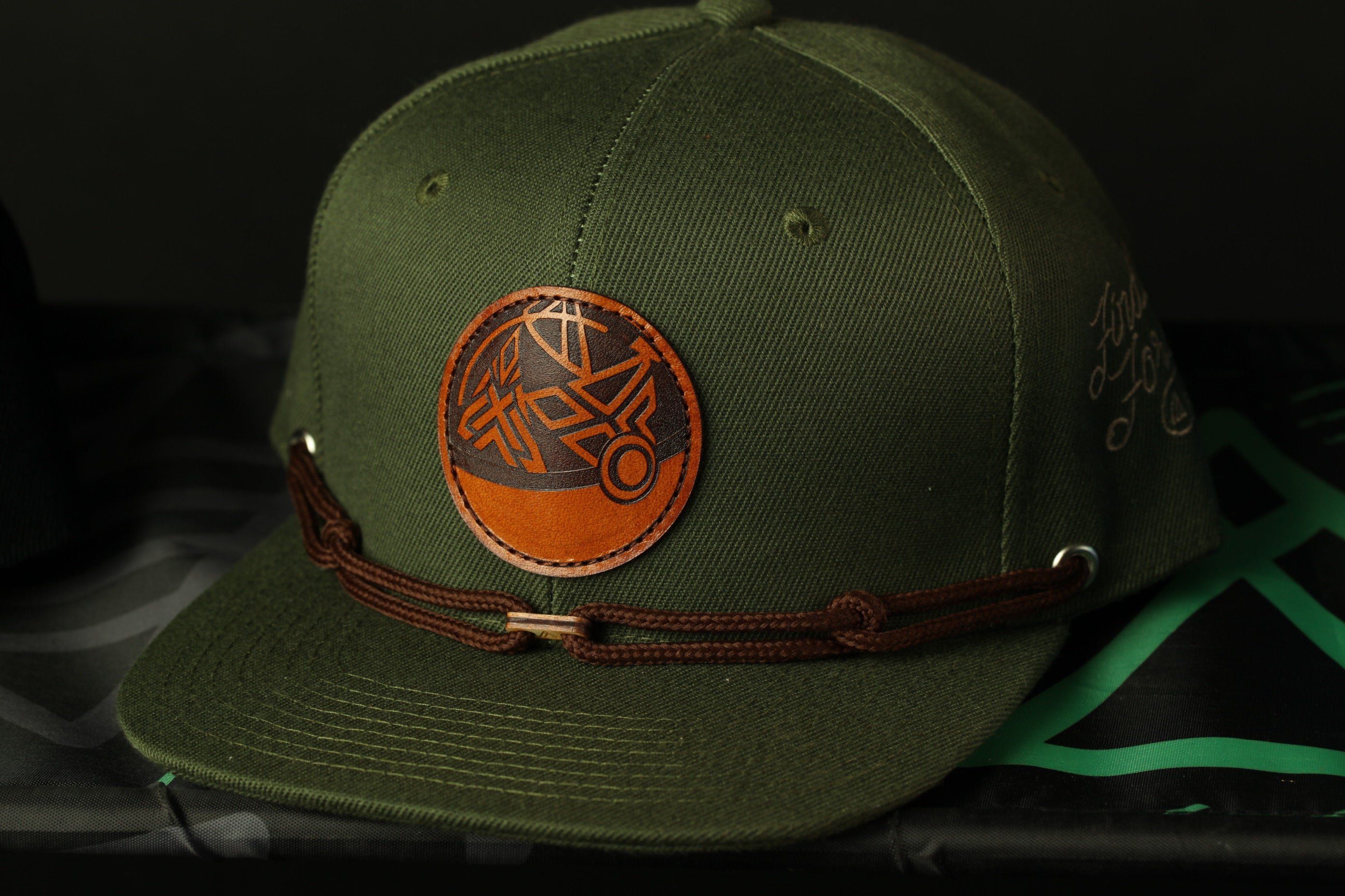 A green baseball cap with a circular logo and a brown leather strap.