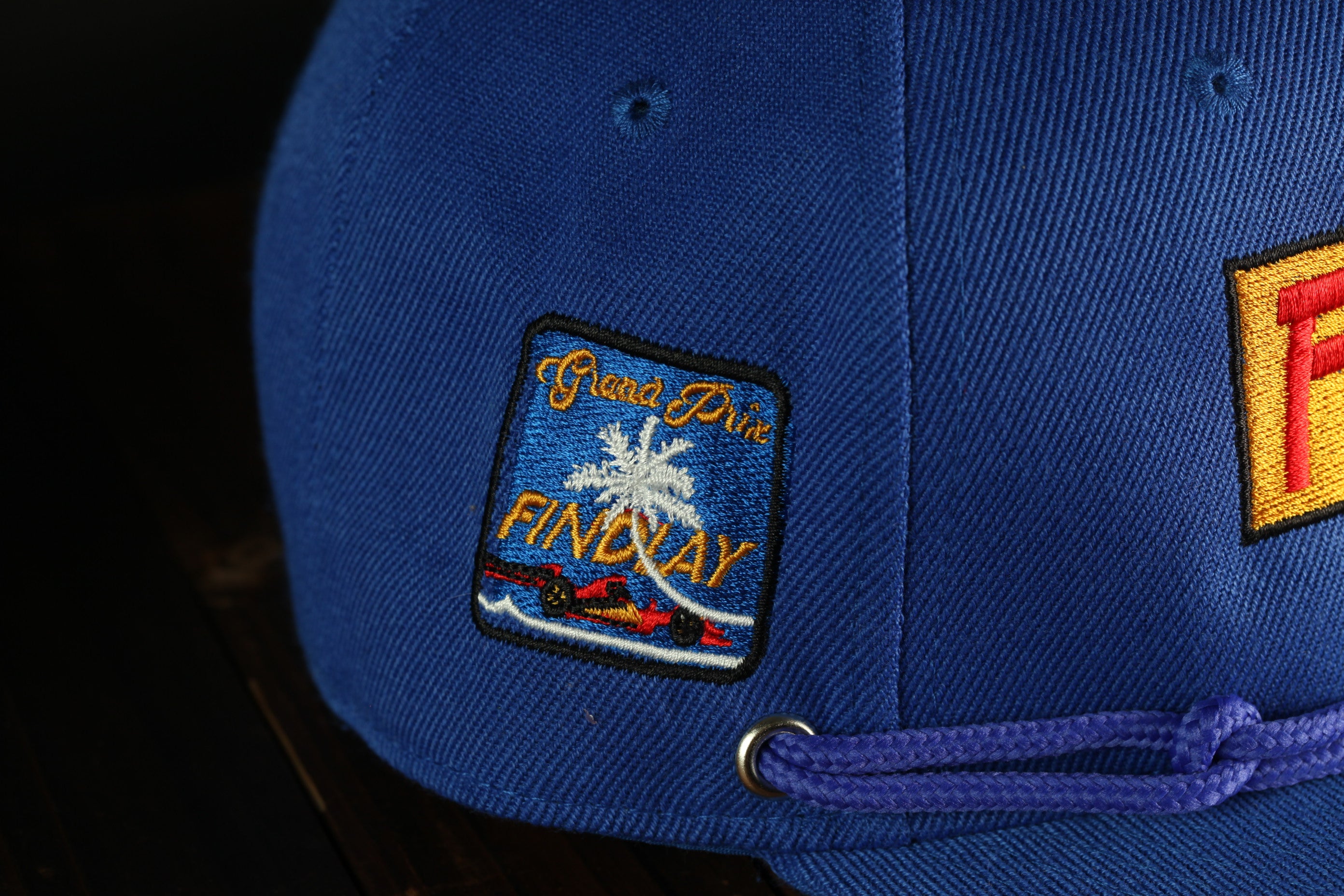 A close-up view of a blue baseball cap with a patch on the front, featuring a palm tree and the text "Findlay".