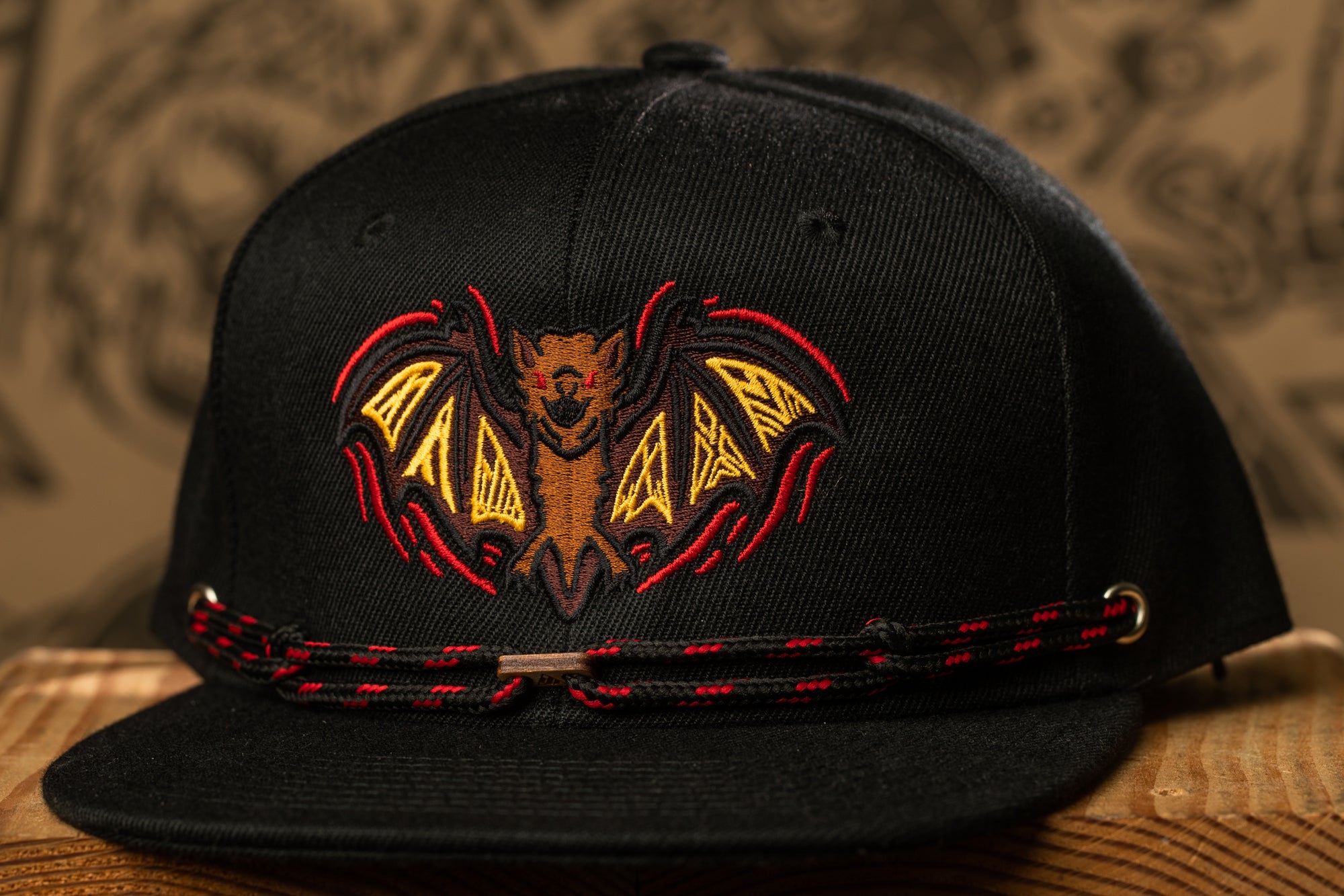 A black baseball cap with a bat embroidered on it, featuring a red and yellow design.