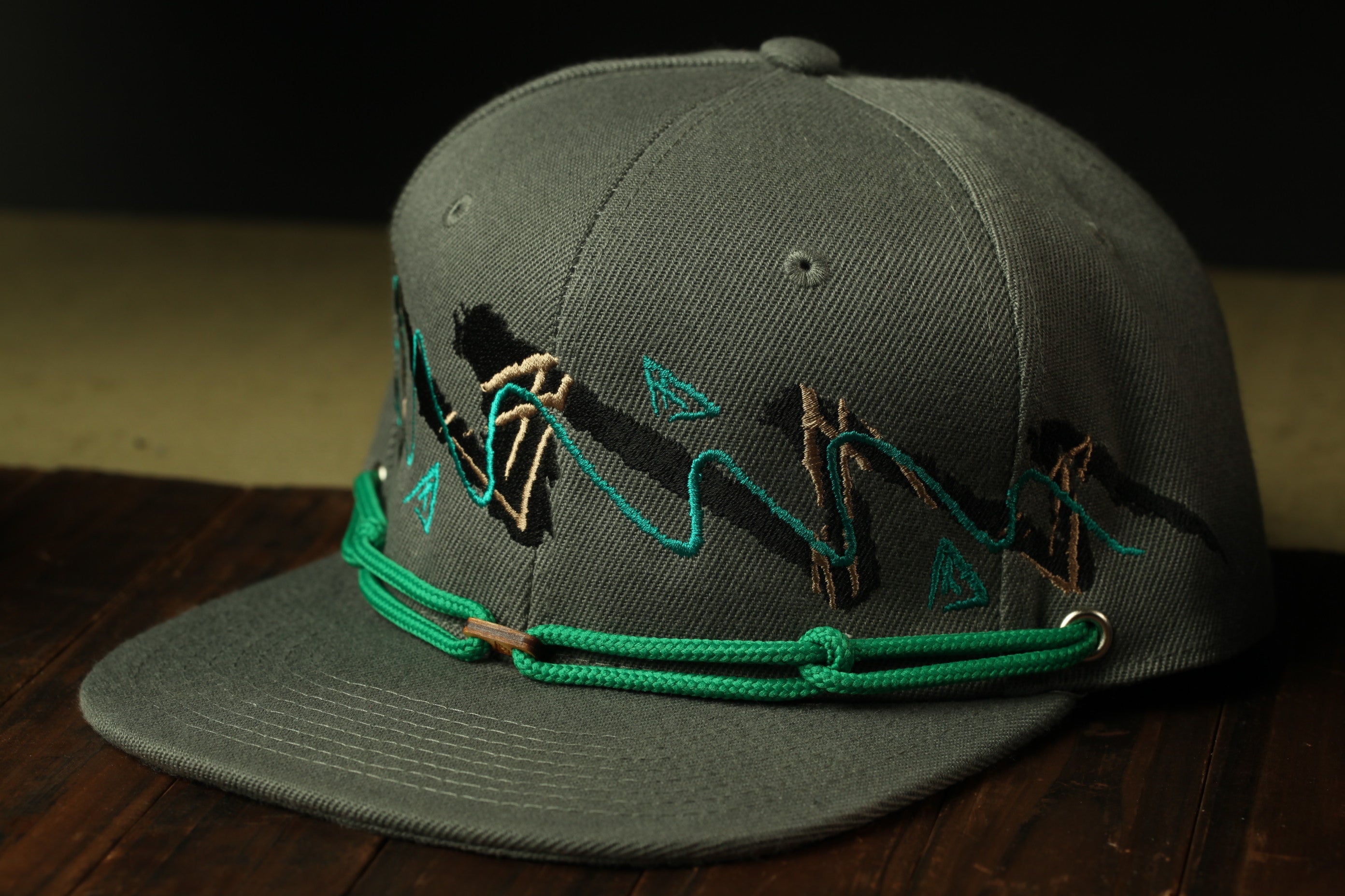A gray baseball cap with a green string and a graphic design on the front.
