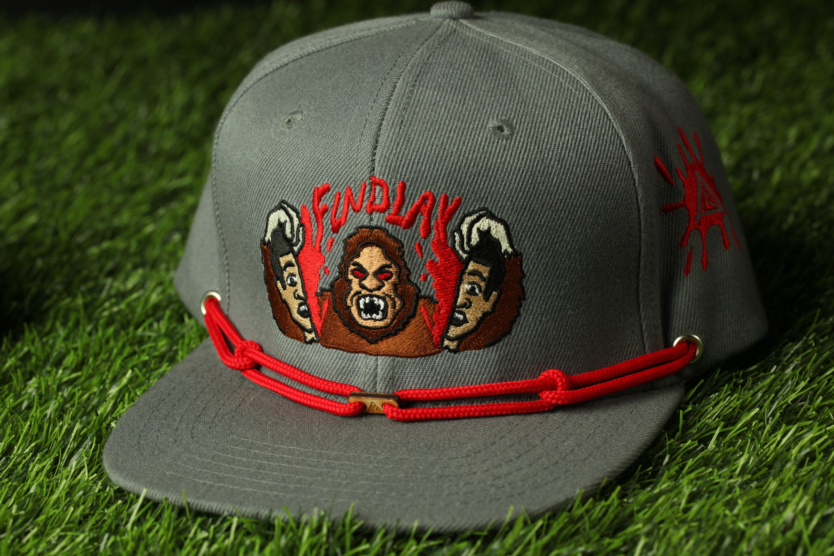 A gray baseball cap with a red string and an embroidered design featuring a cartoon character.