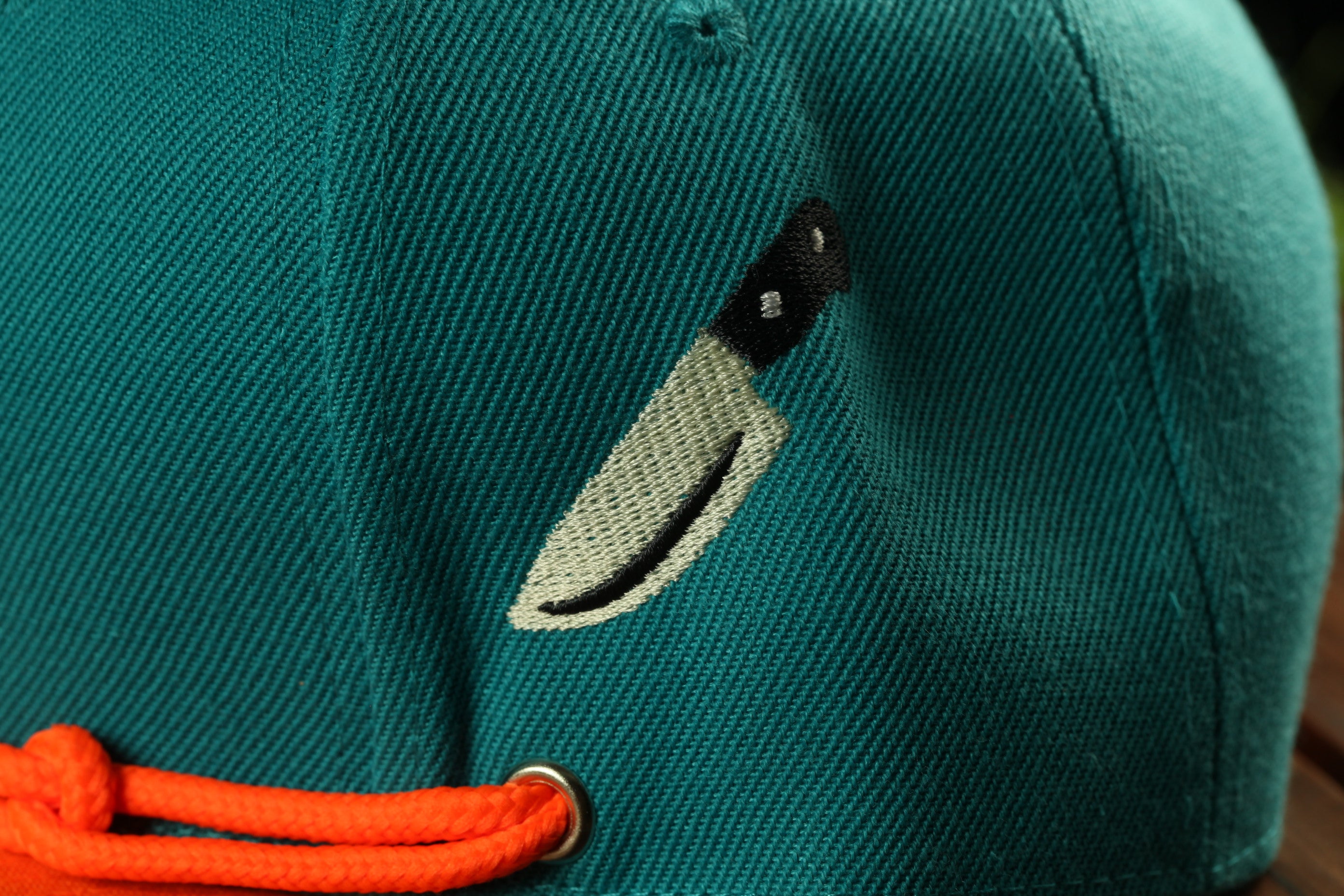 A close-up view of a green baseball cap with a black and white embroidered knife design on the front.