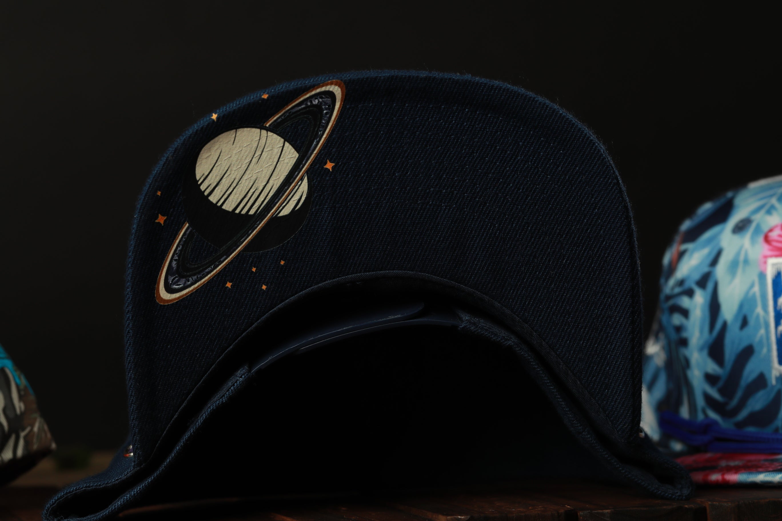 A dark blue baseball cap with a planet design on the front, sitting on a wooden surface.