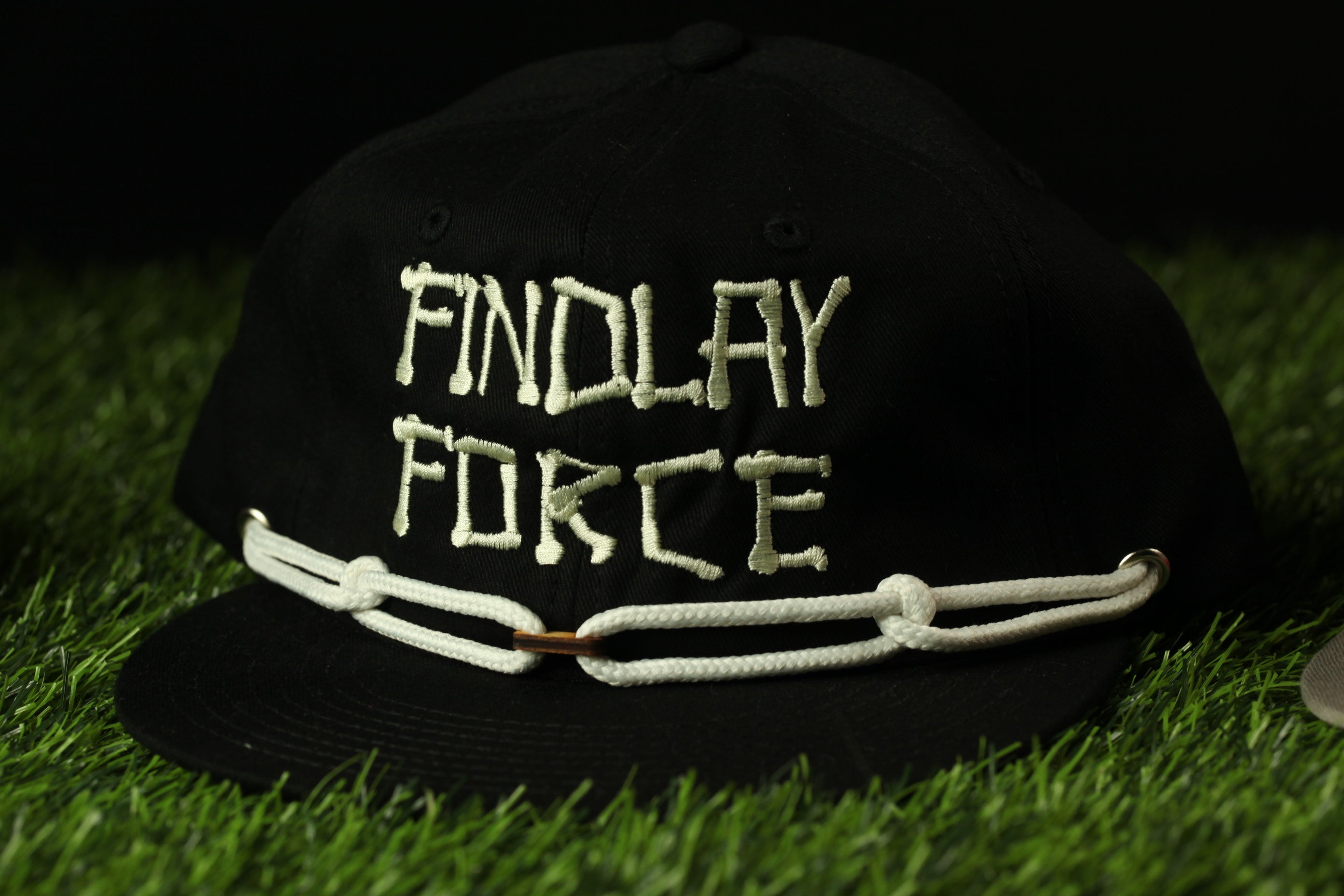 A black baseball cap with white text on it, lying on a grassy surface.