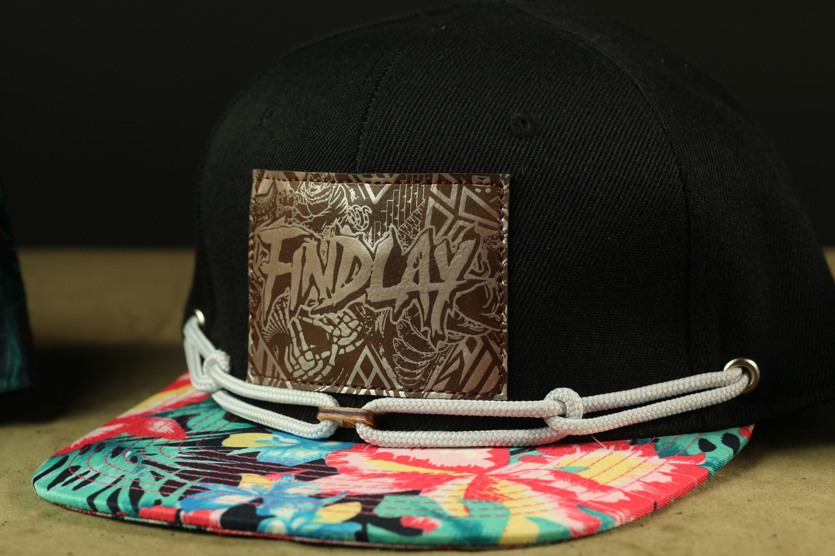 A black baseball cap with a colorful floral pattern and a patch on the front displaying the word "FINDlay".