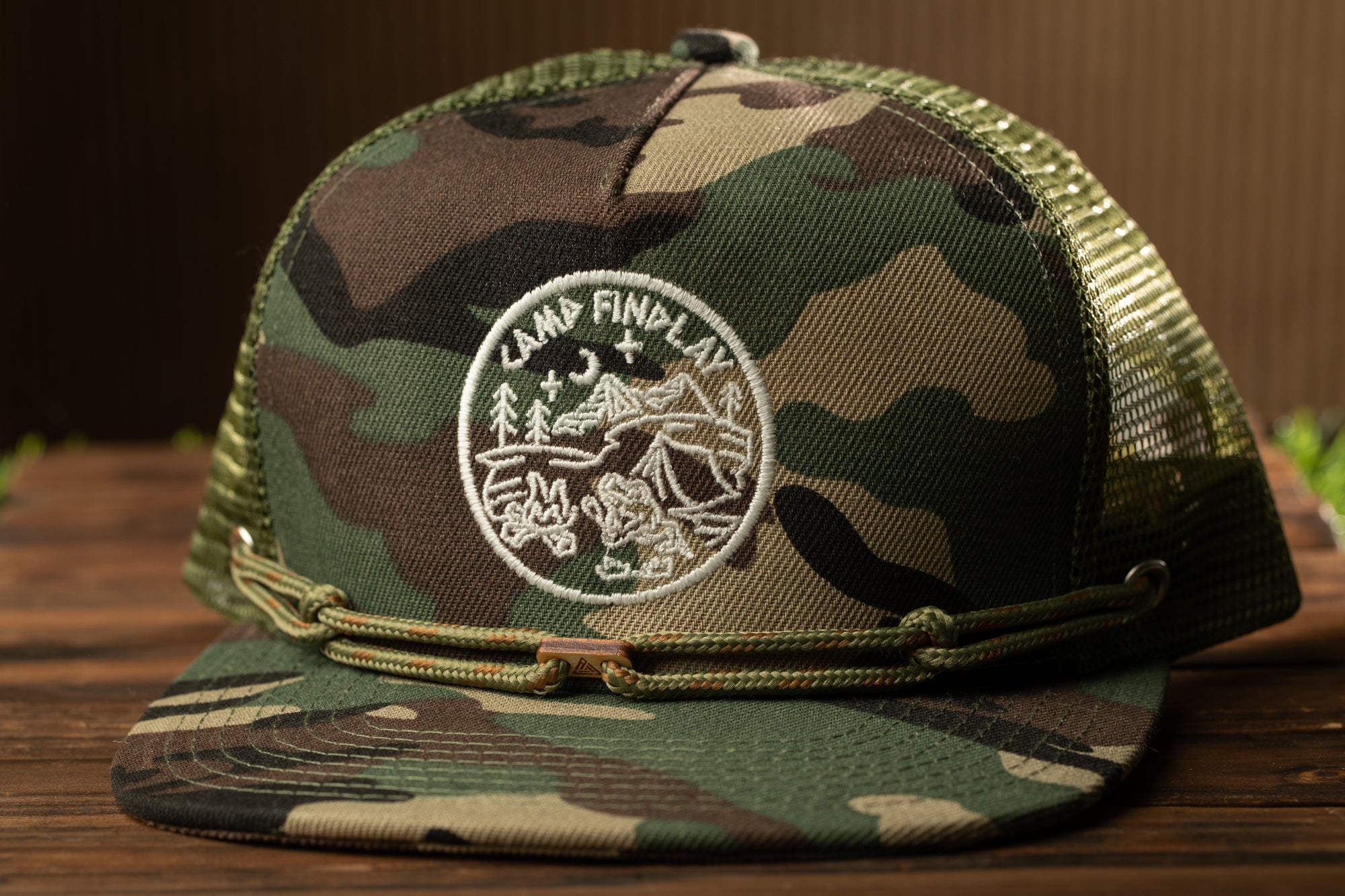 A camouflage baseball cap with a logo on the front, sitting on a wooden surface.