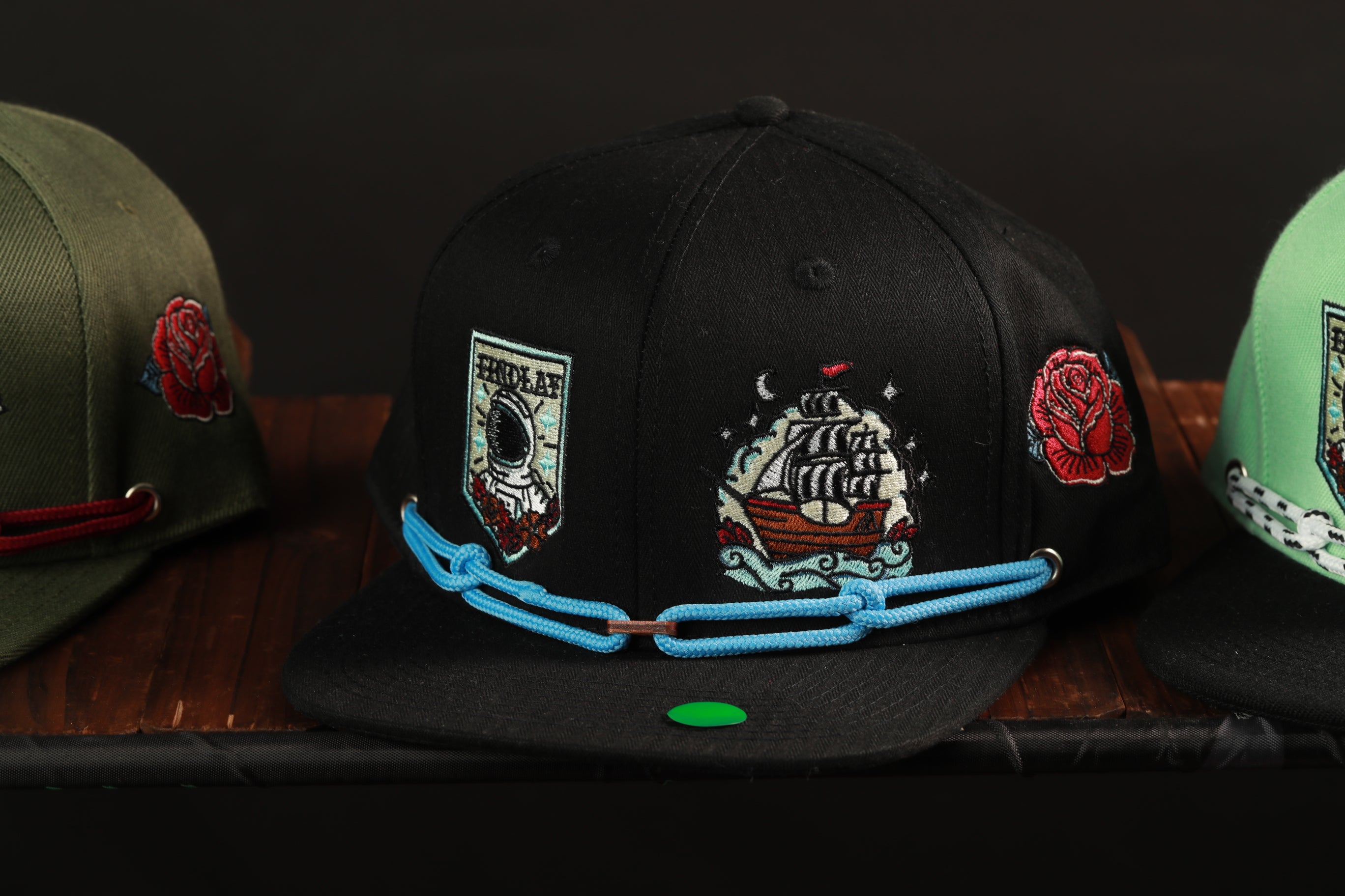 A close-up image of three baseball caps with various embroidered designs, including a ship, a rose, and other decorative elements.
