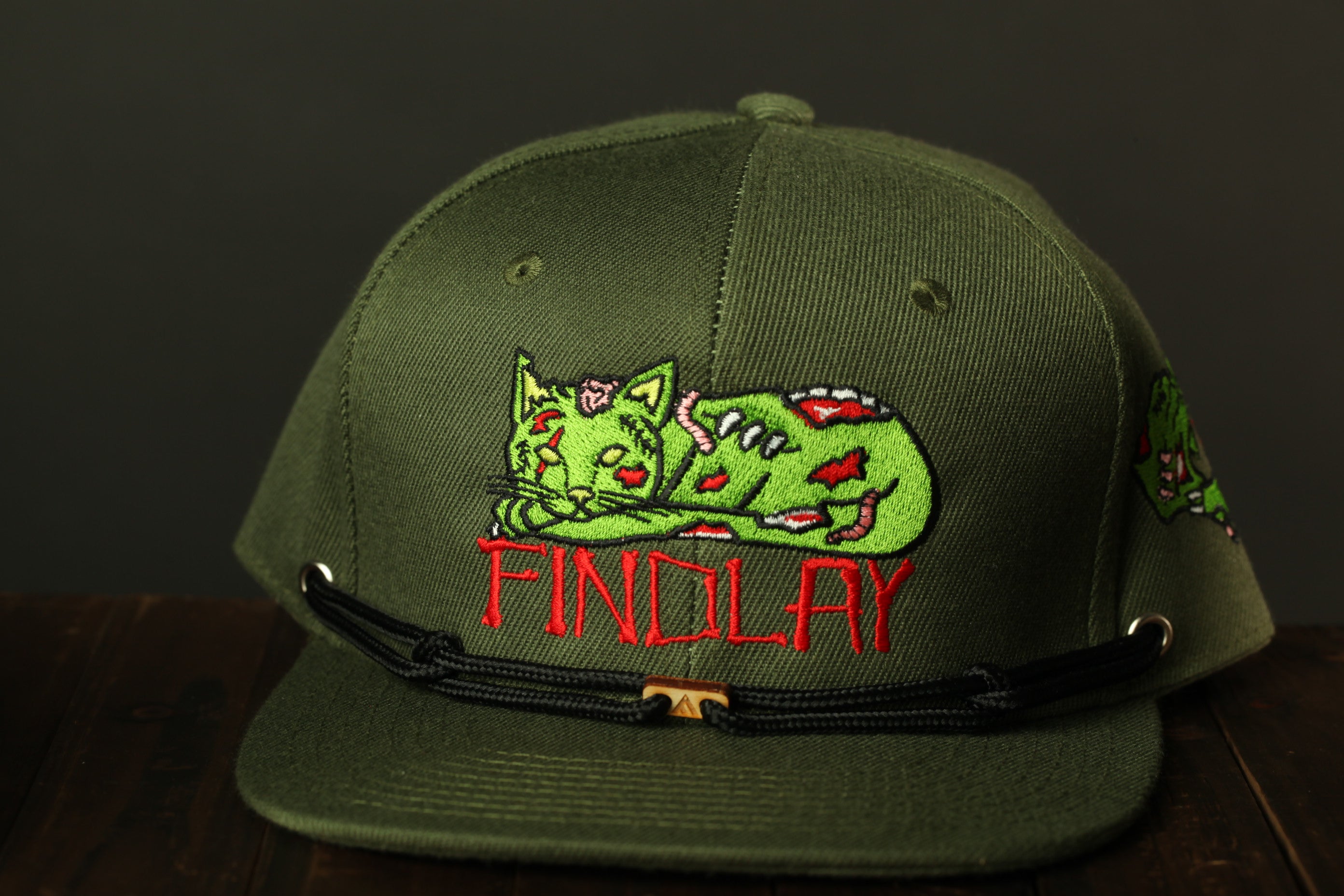 A green baseball cap with a graphic of a green cat and the word "FINDLAY" printed on it.