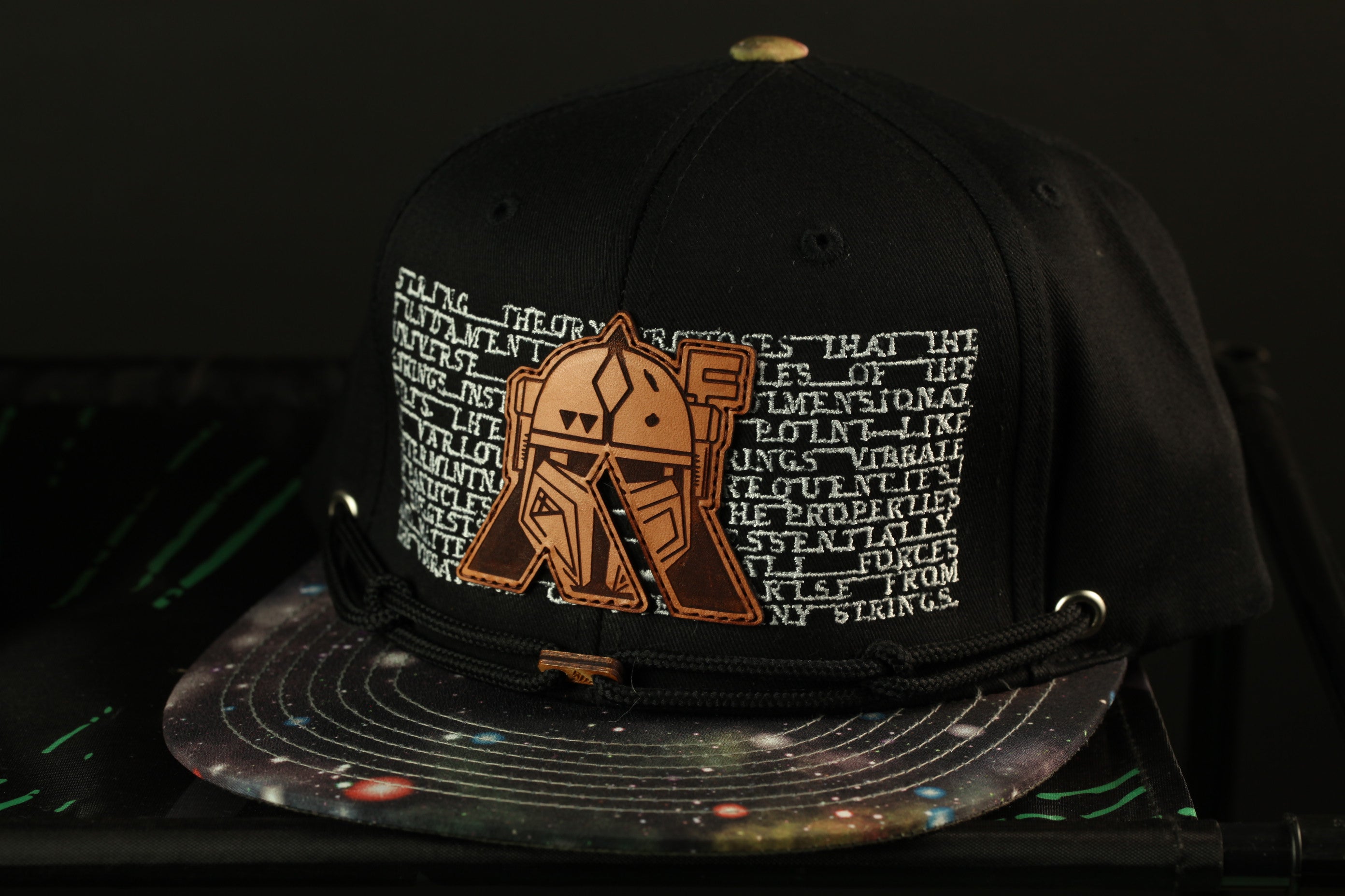 A black baseball cap with a space-themed design and a patch featuring a robot or character.