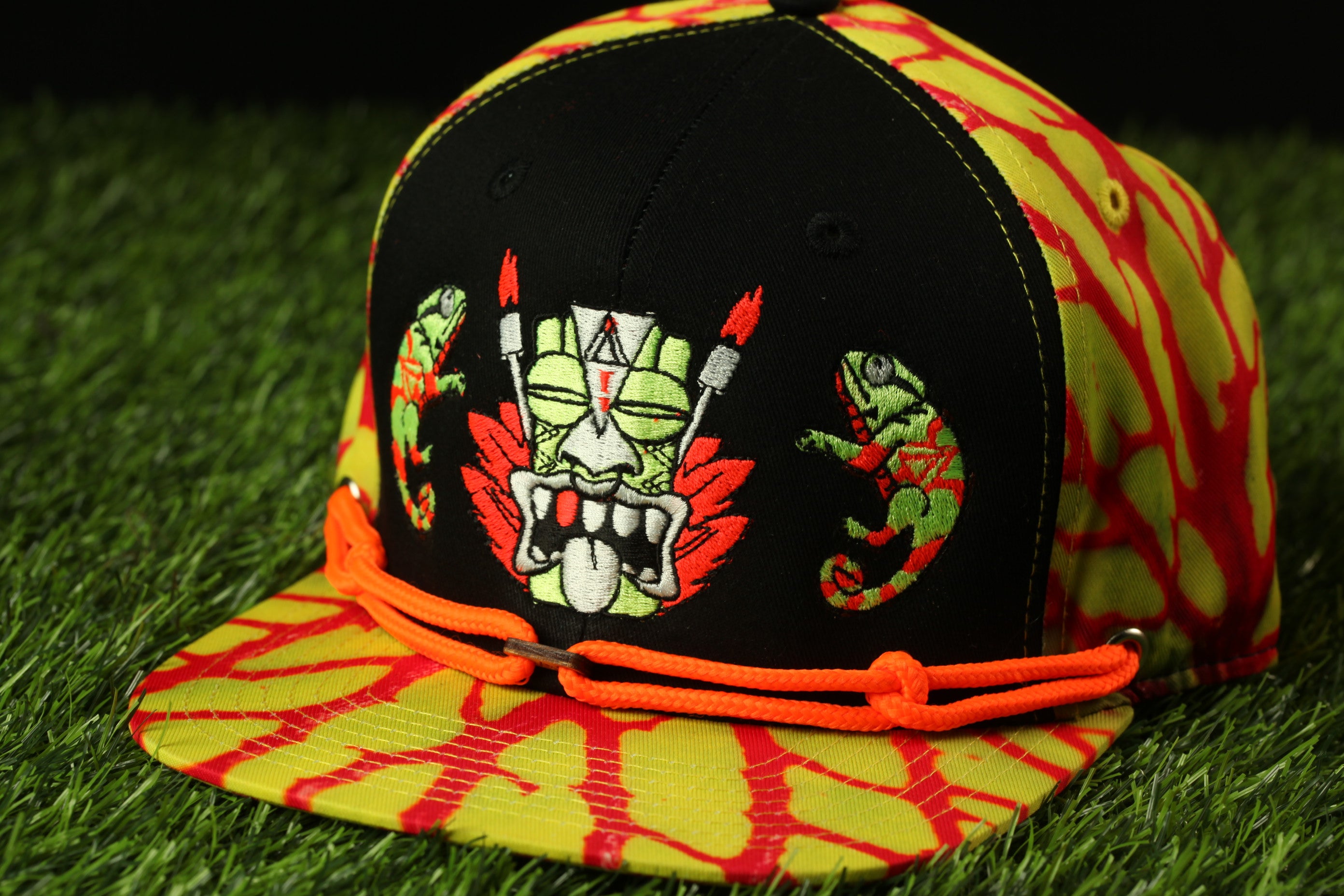A colorful baseball cap with a graphic design featuring a mask and two chameleons.