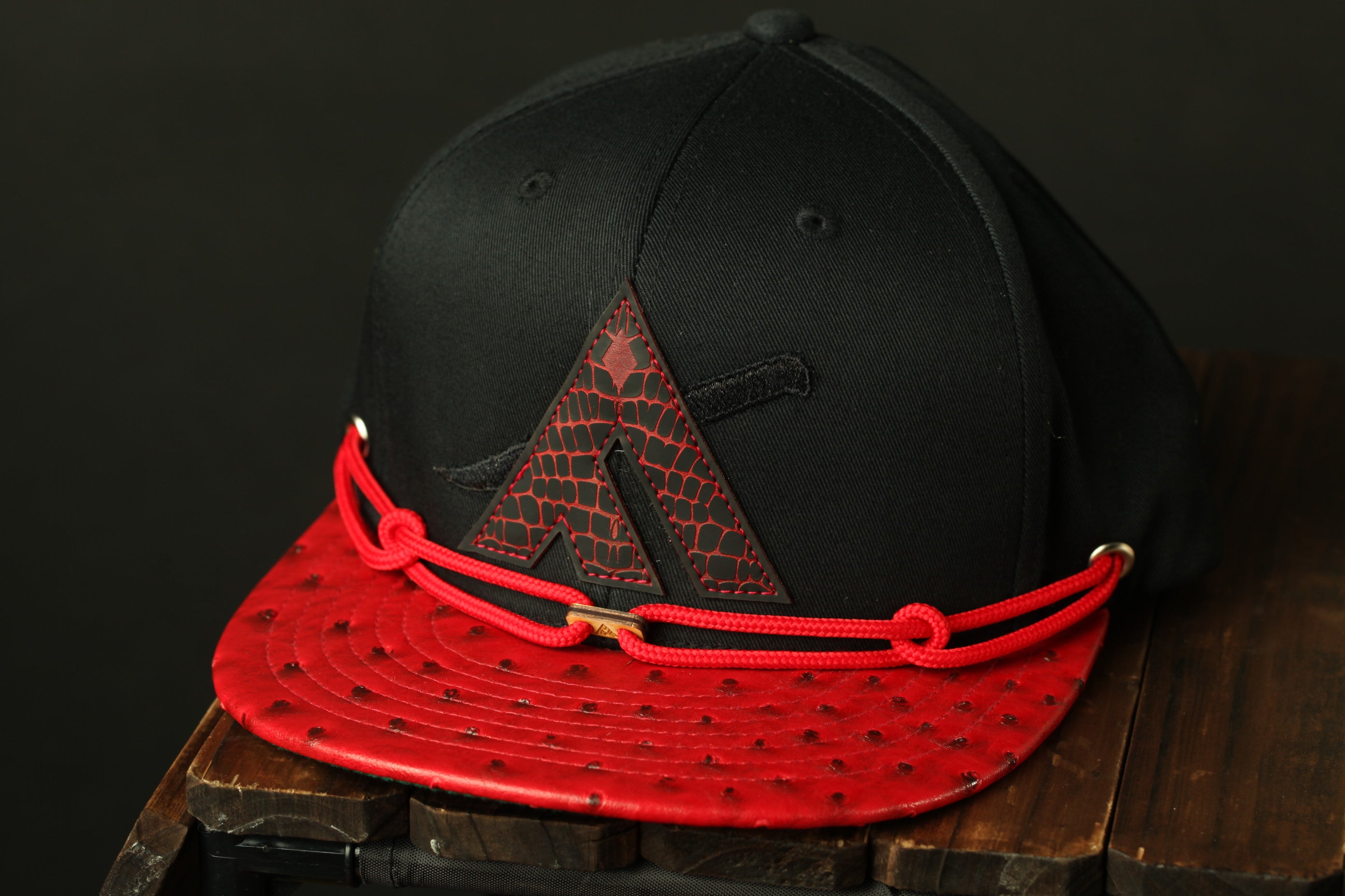 A black baseball cap with a red brim and a red string around the brim, placed on a wooden surface.