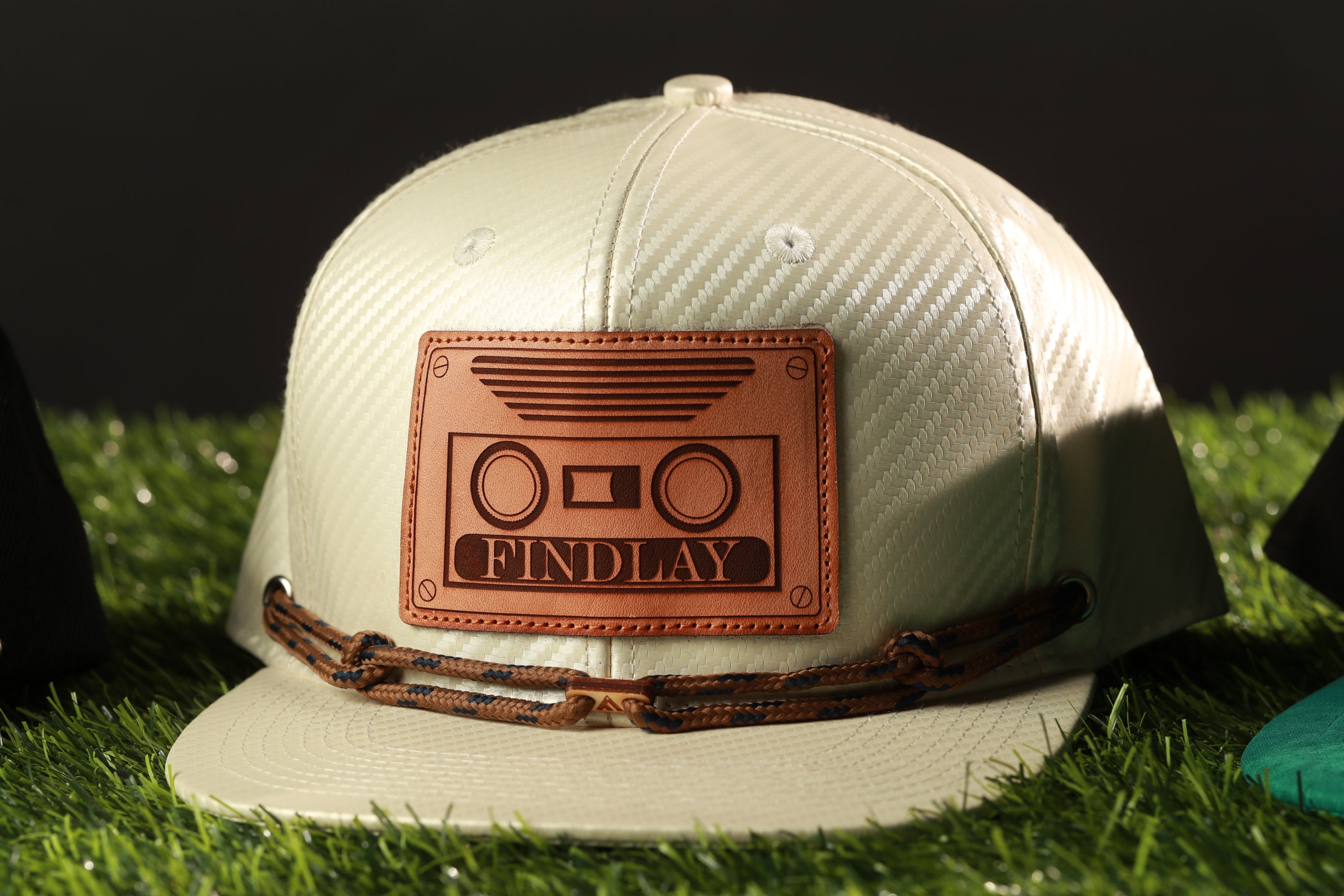 A white baseball cap with a leather patch on it, featuring the word "FINDLAY" printed on it.