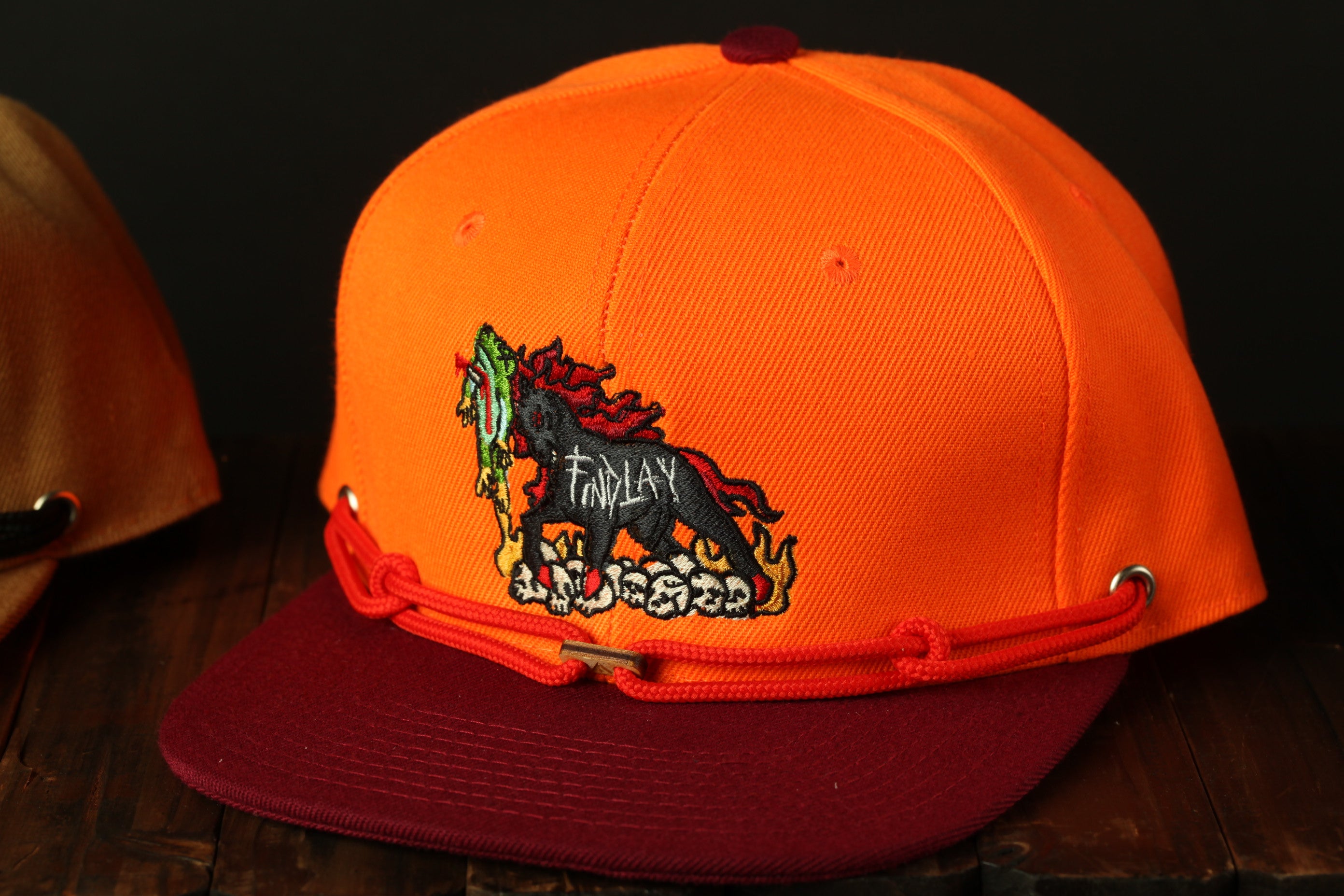 An orange baseball cap with a red band and a black and red embroidered logo on the front.