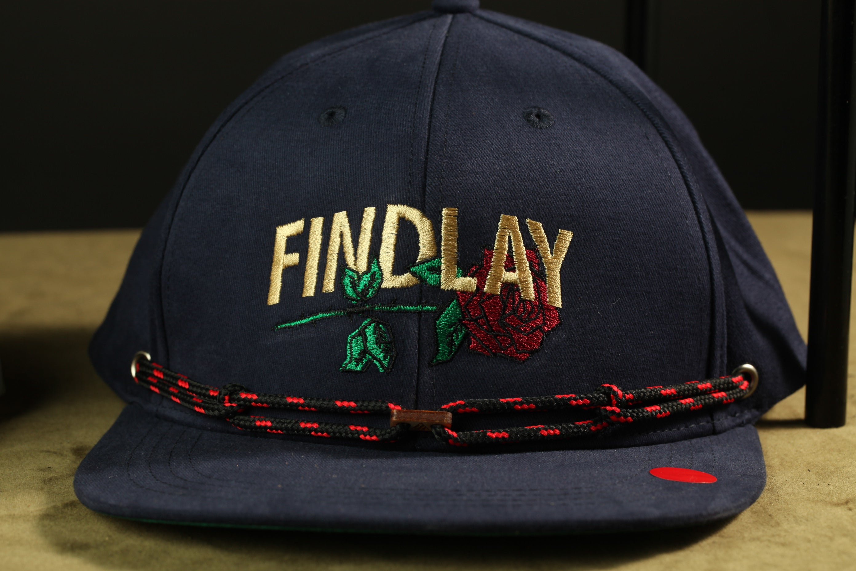 A navy blue baseball cap with the word "FINDlay" embroidered on it, along with a red rose and green leaves.