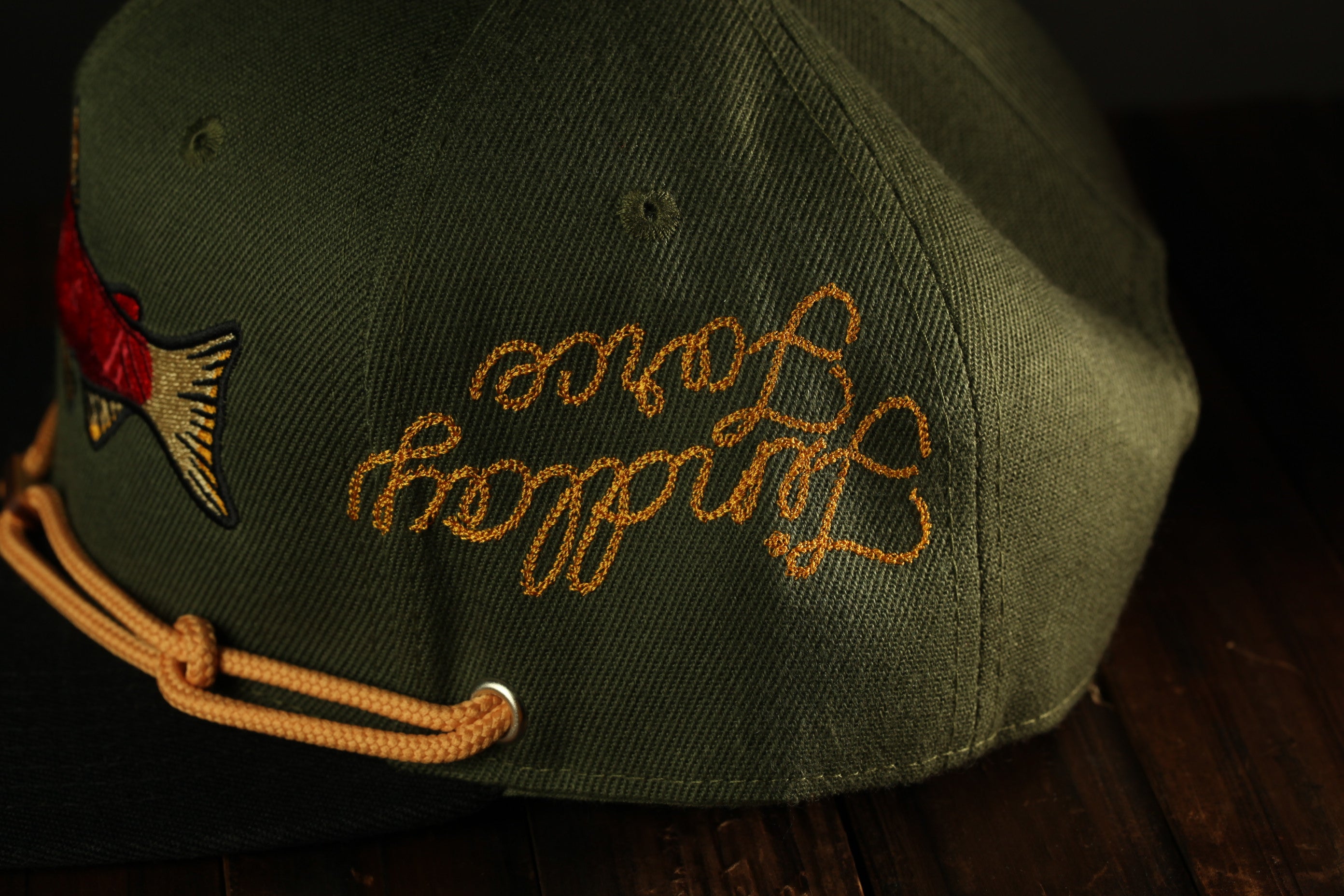 A close-up view of a green baseball cap with a yellow embroidered phrase on the back.