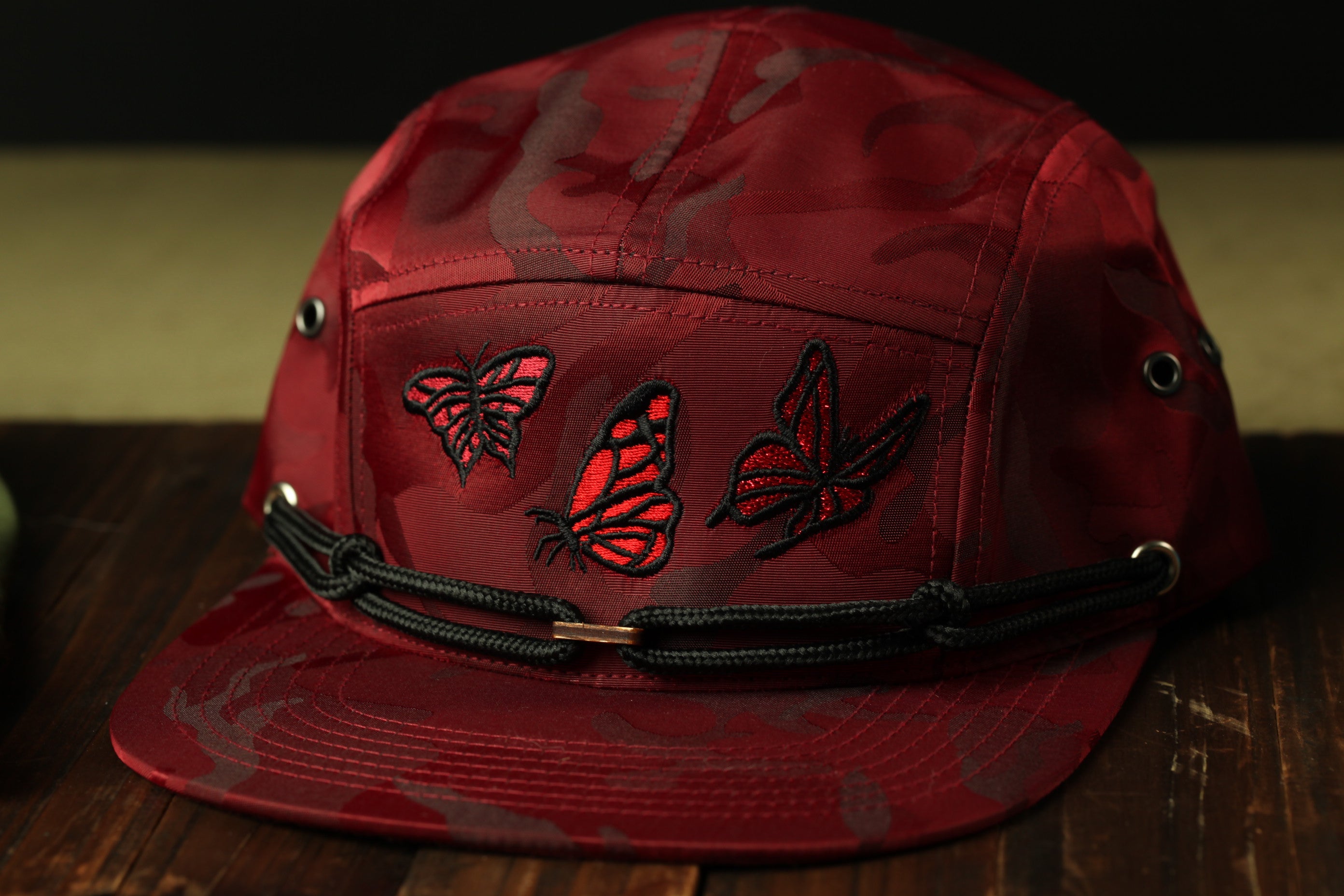 A red camouflage baseball cap with three red butterfly embroidered designs on the front.