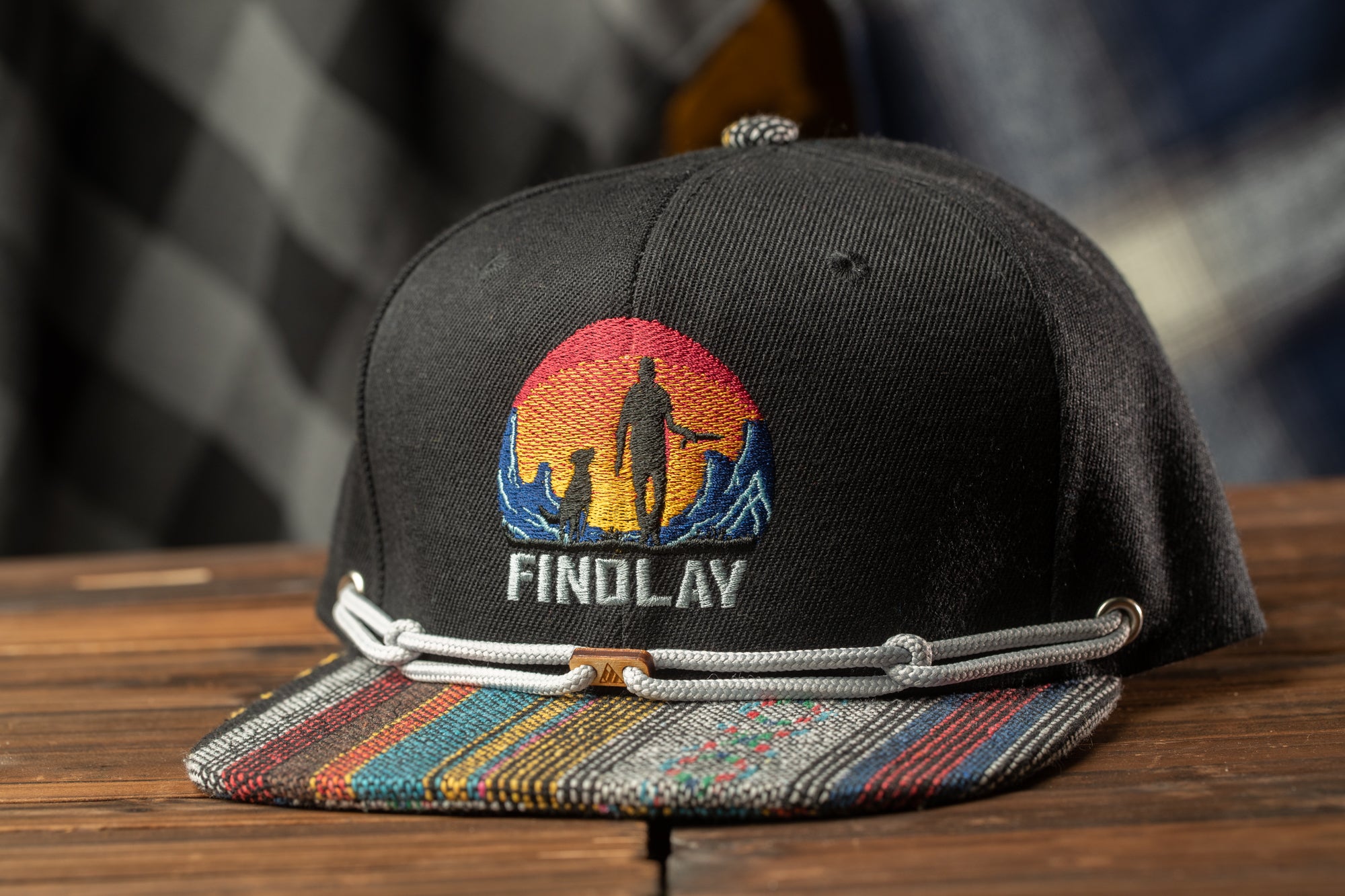 A black baseball cap with a colorful, embroidered design on the front, featuring a silhouette of a person and mountains.