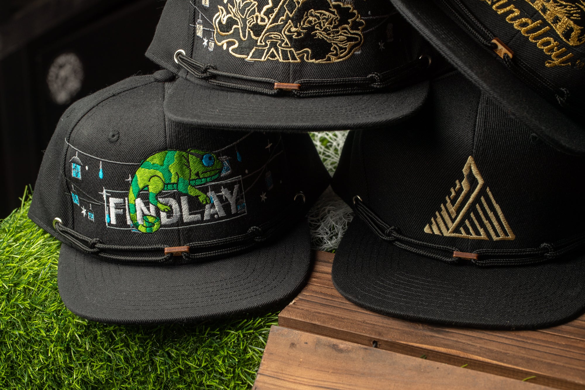 A collection of black baseball caps with various designs and text, including a cap with a green chameleon and the word "FINDLAY".