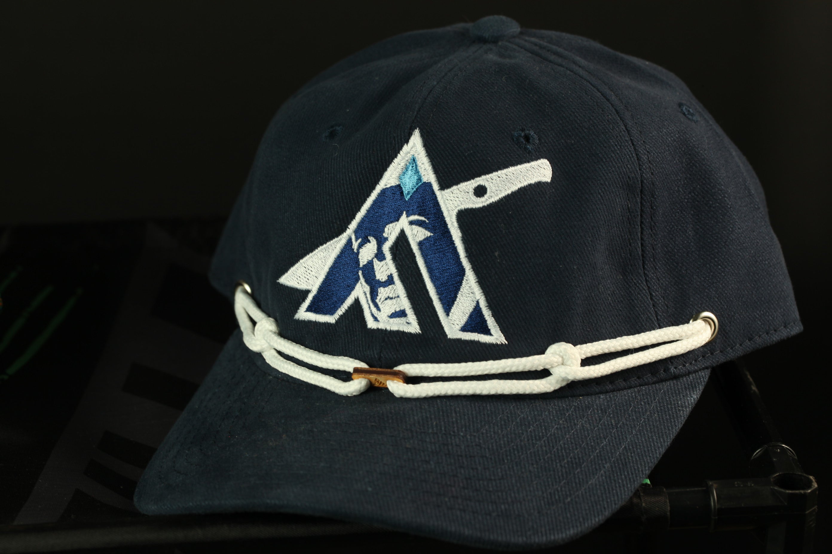 A navy blue baseball cap with a white chain strap and a logo on the front.