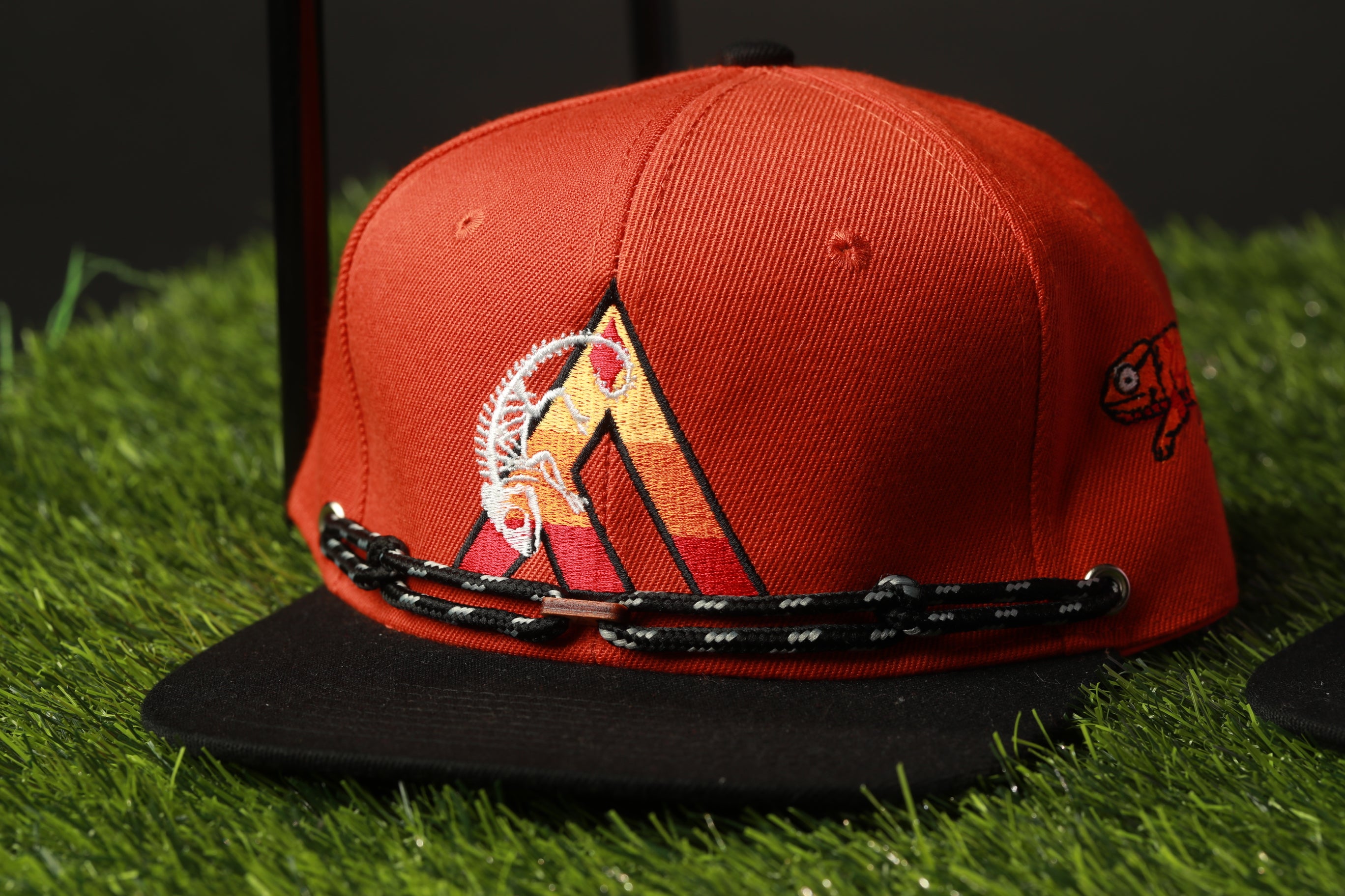 A red baseball cap with a black brim and a black chain strap, placed on a grassy surface.