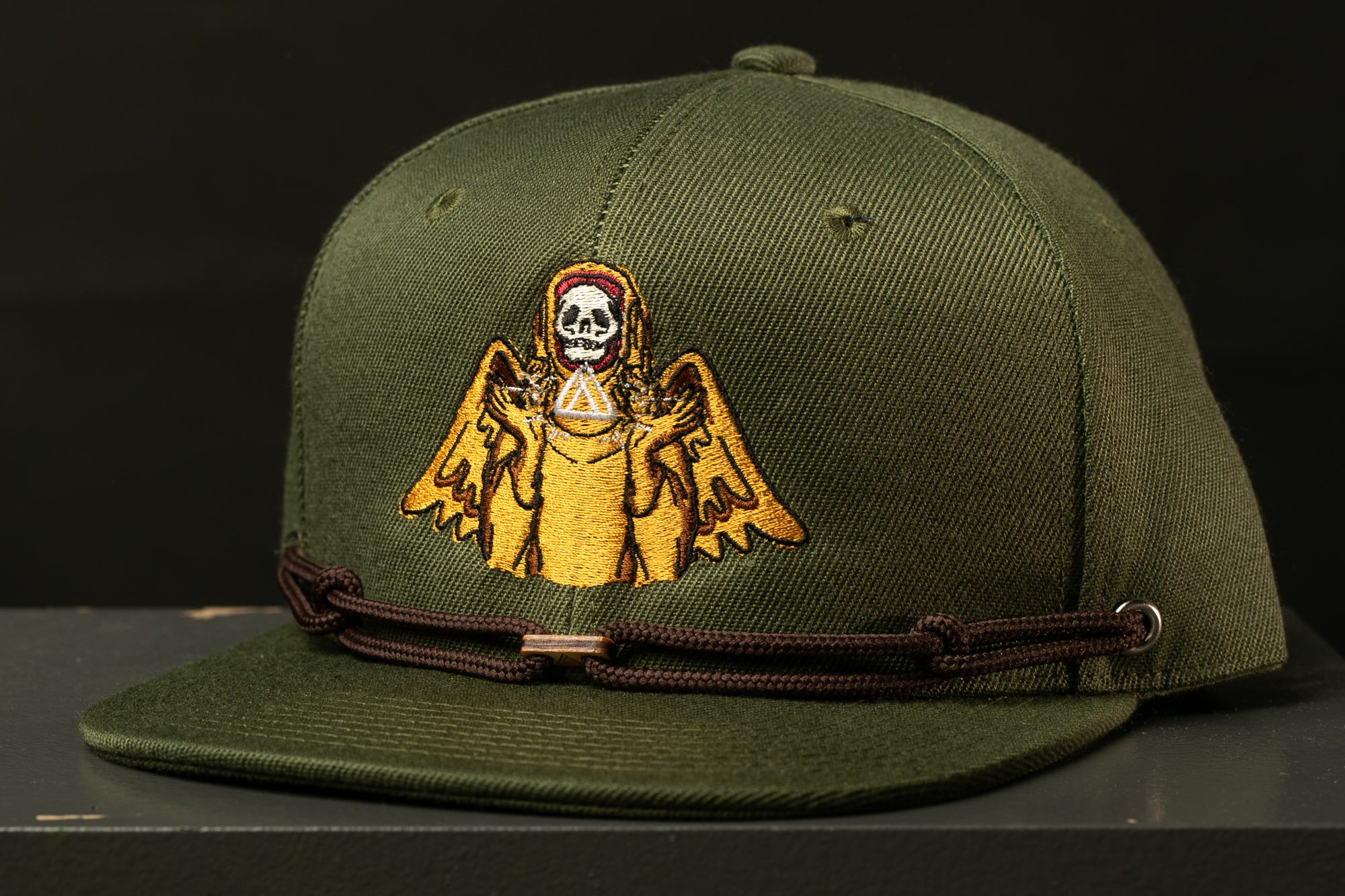 A green baseball cap with a skull and winged figure embroidered on it.
