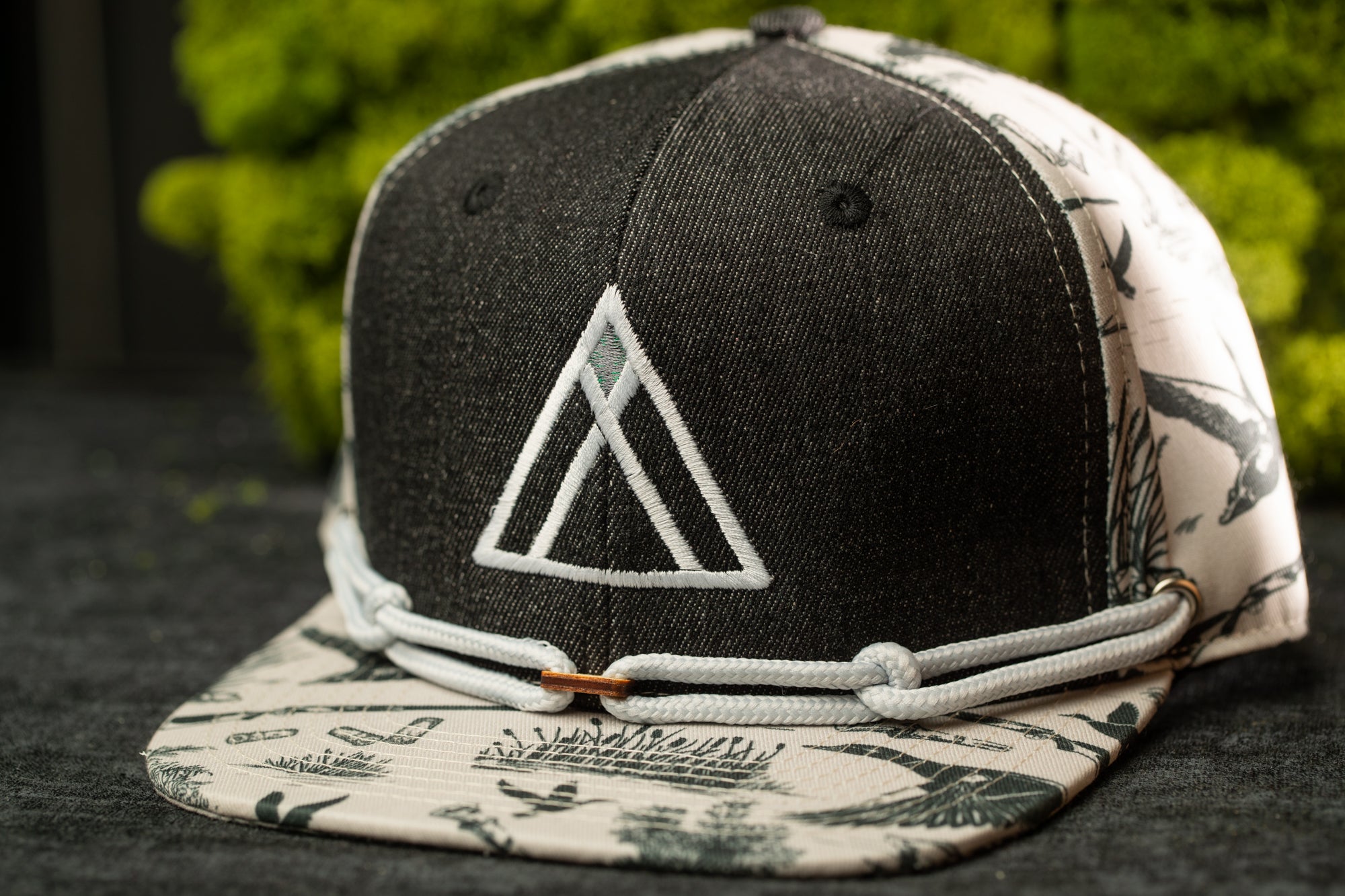 A black and white baseball cap with a white triangle logo on the front, placed on a surface with a green plant in the background.