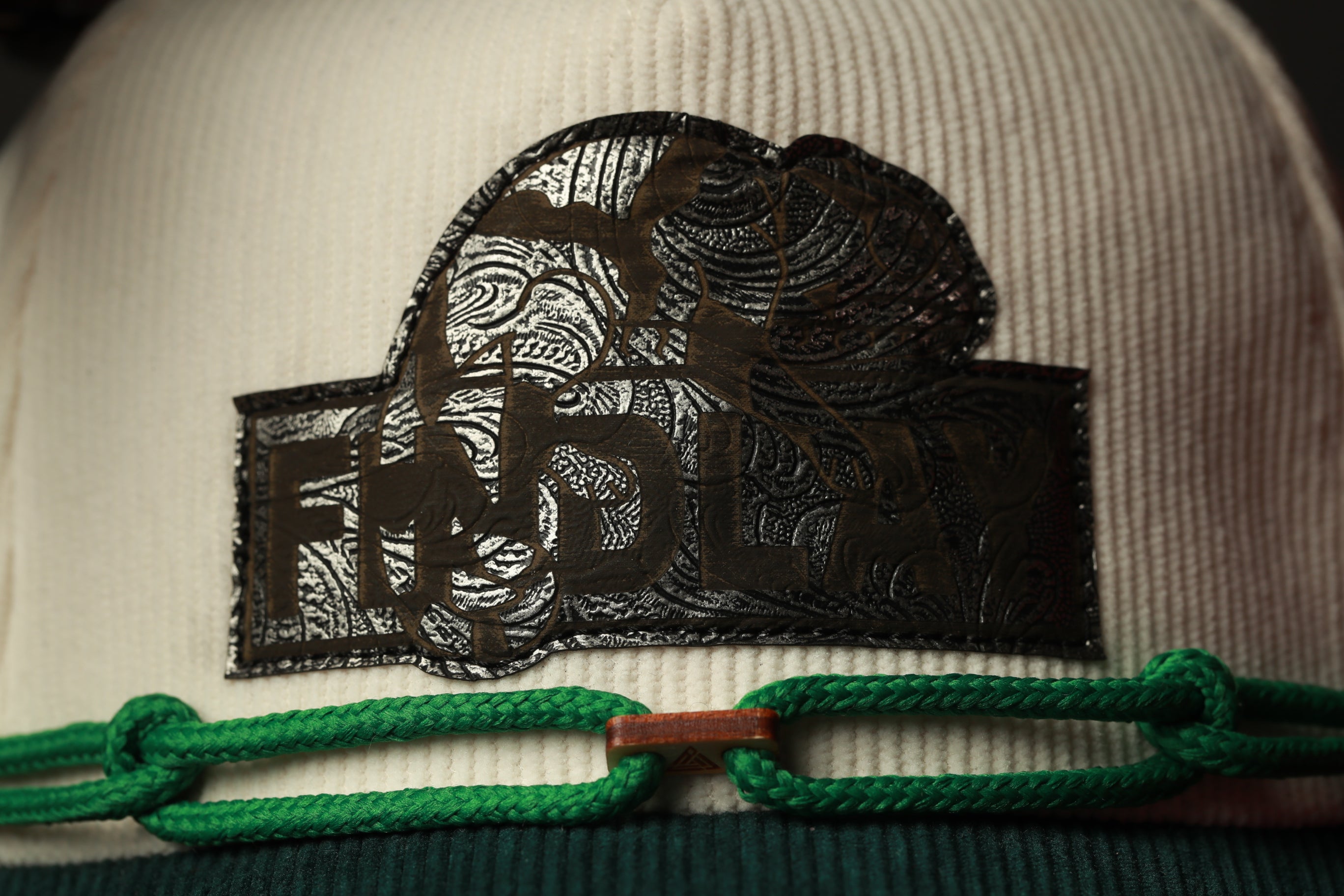 A close-up view of a white hat with a black and green decorative element on the front.