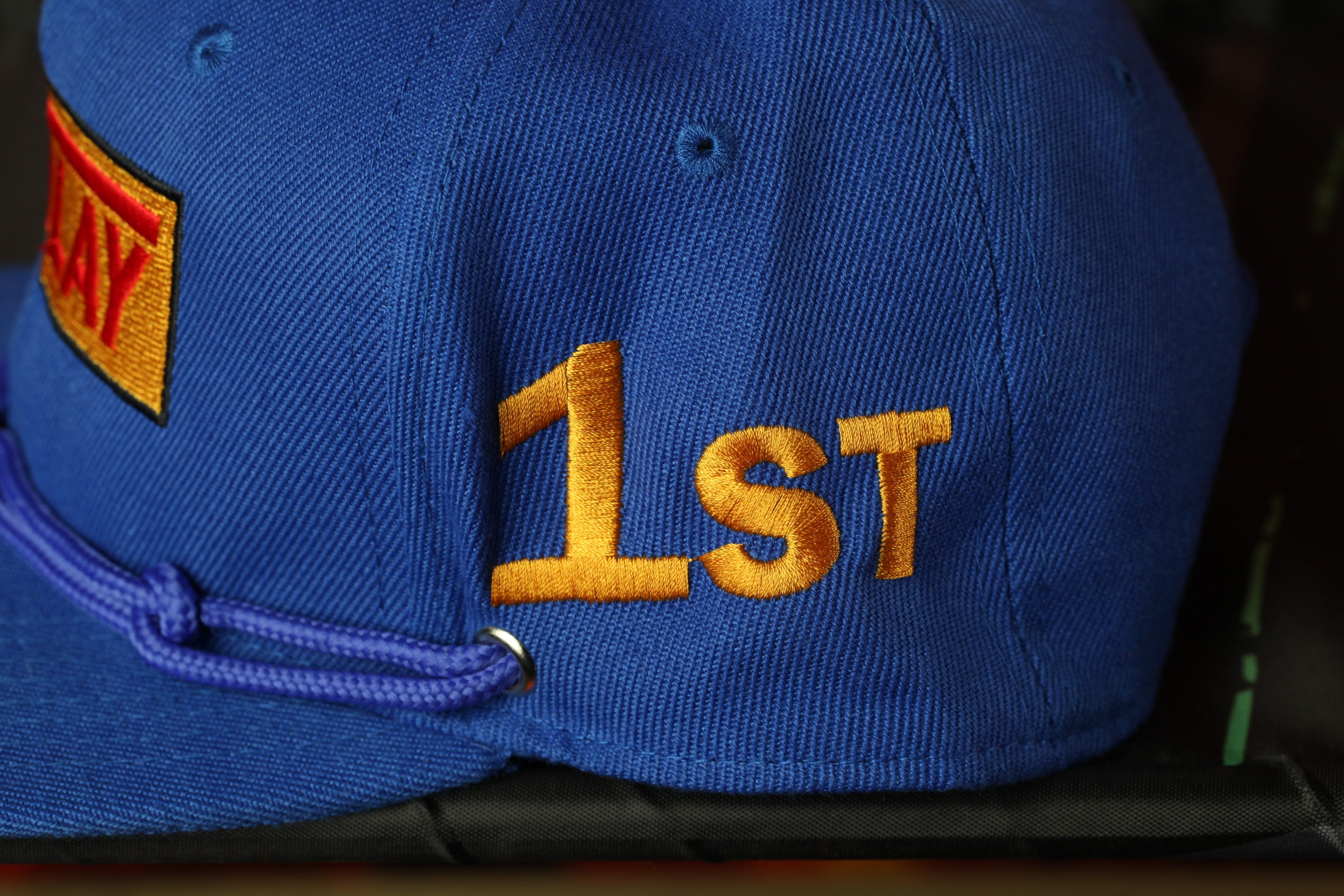 A close-up view of a blue baseball cap with the number "1st" embroidered on it.
