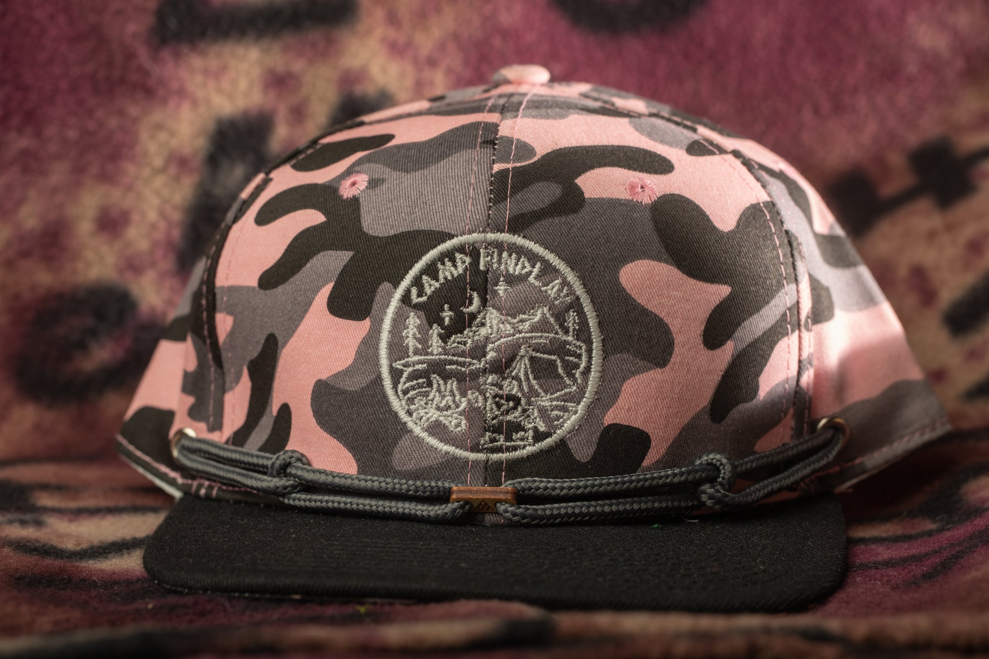 A camouflage baseball cap with a circular embroidered logo on the front.