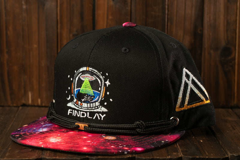 A black baseball cap with a colorful galaxy print and a space-themed design, featuring a small alien figure and the text "FINDLAY".