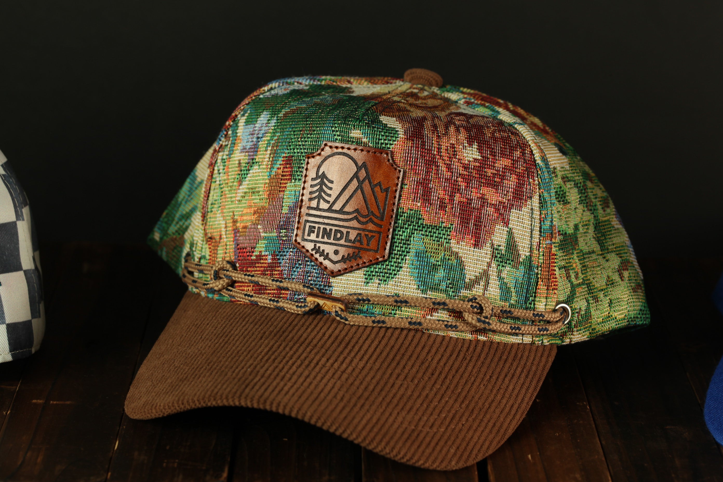 A colorful, patterned baseball cap with a leather patch and a woven brim, sitting on a wooden surface.