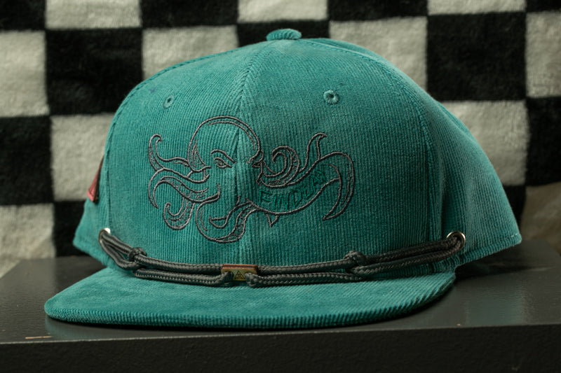 A teal-colored baseball cap with an embroidered design of an octopus on the front.