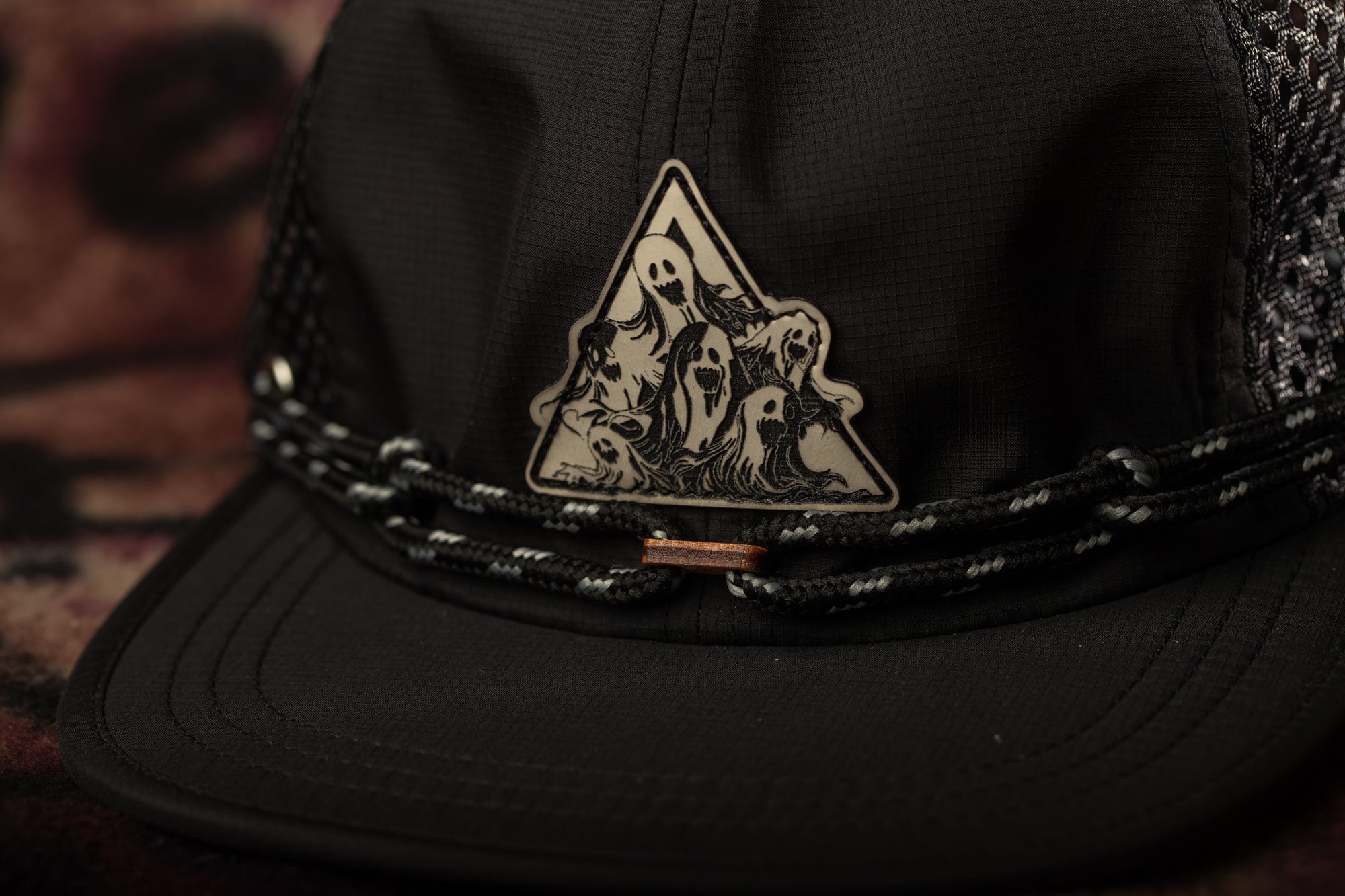 A close-up view of a black baseball cap with a triangular emblem featuring a group of ghostly figures.