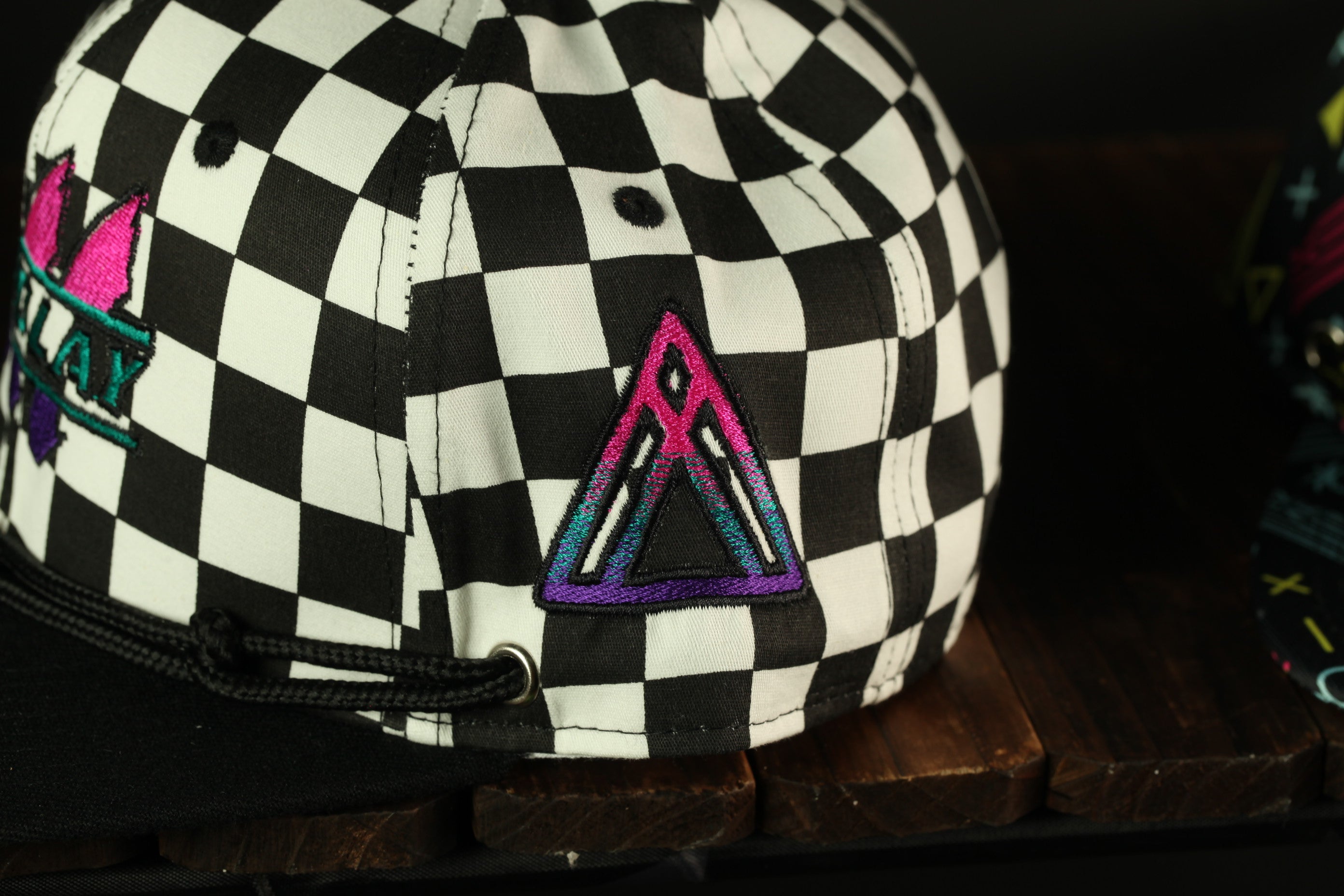 A close-up view of a black and white checkered baseball cap with a colorful triangle-shaped logo on the front.