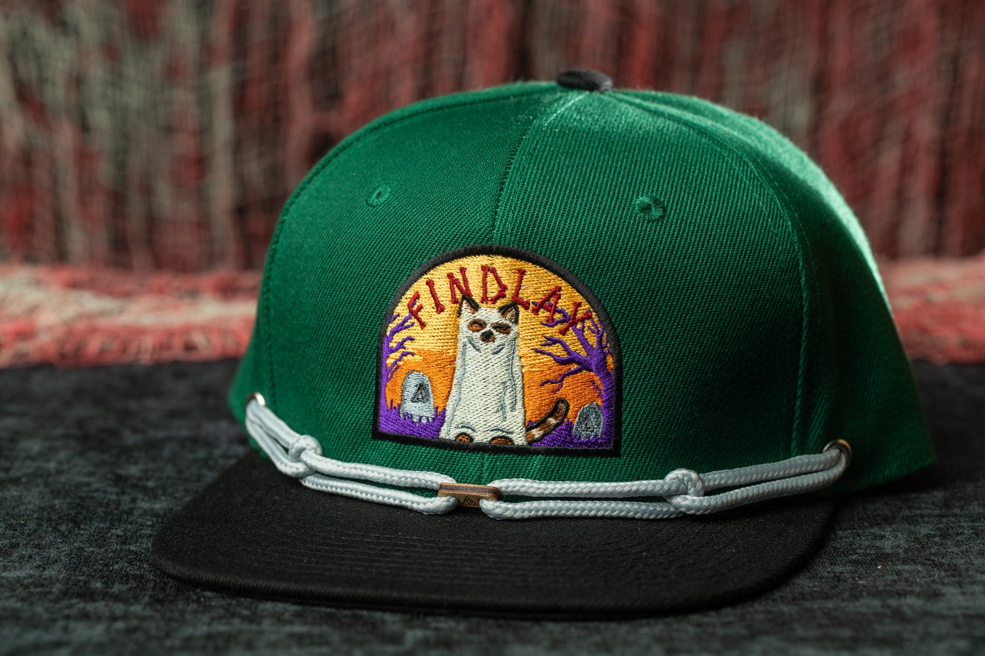 A green baseball cap with a colorful patch on the front, featuring a cartoon character and the text "FIND A FINE FUR".