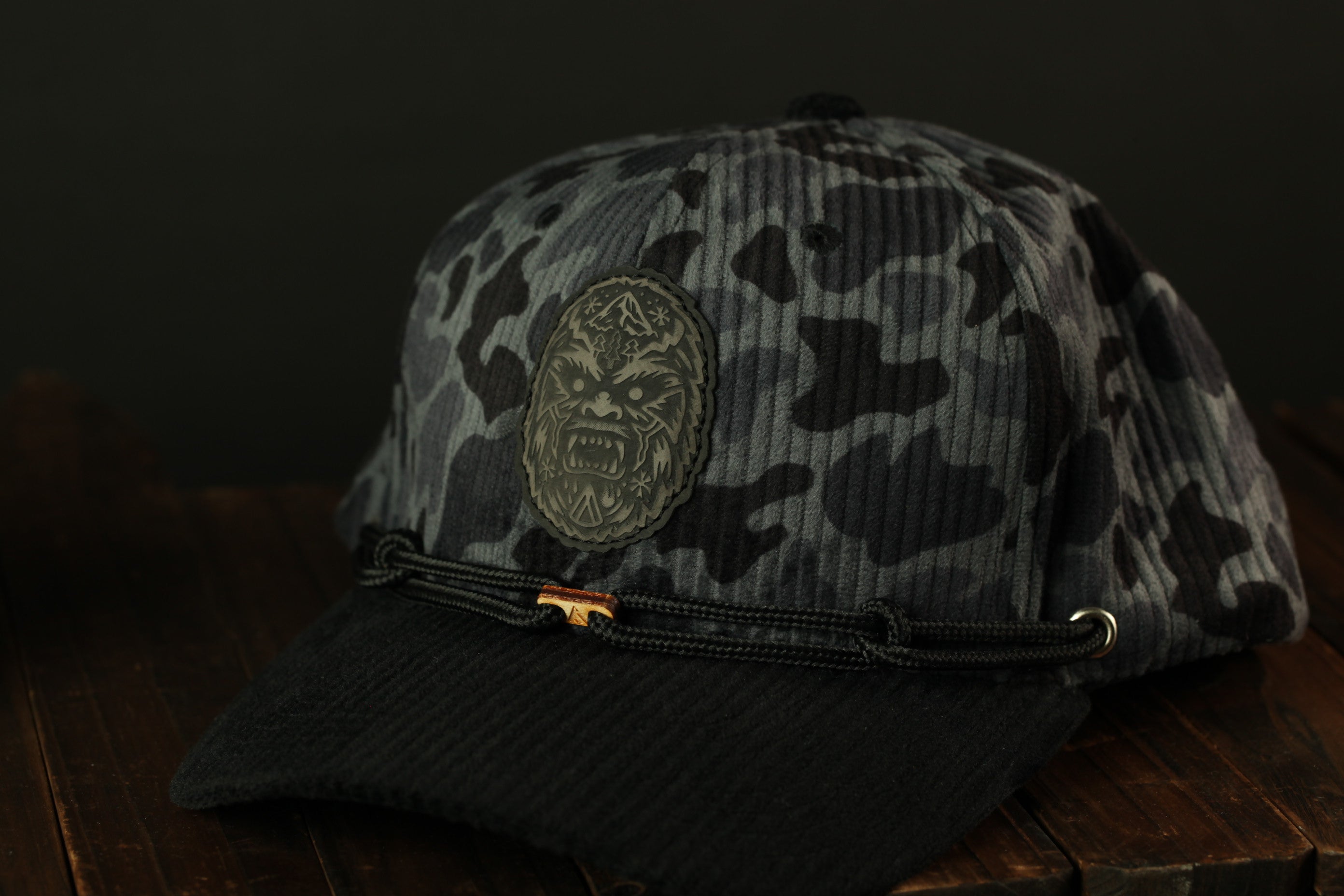 A camouflage baseball cap with a lion's head patch on the front, resting on a wooden surface.