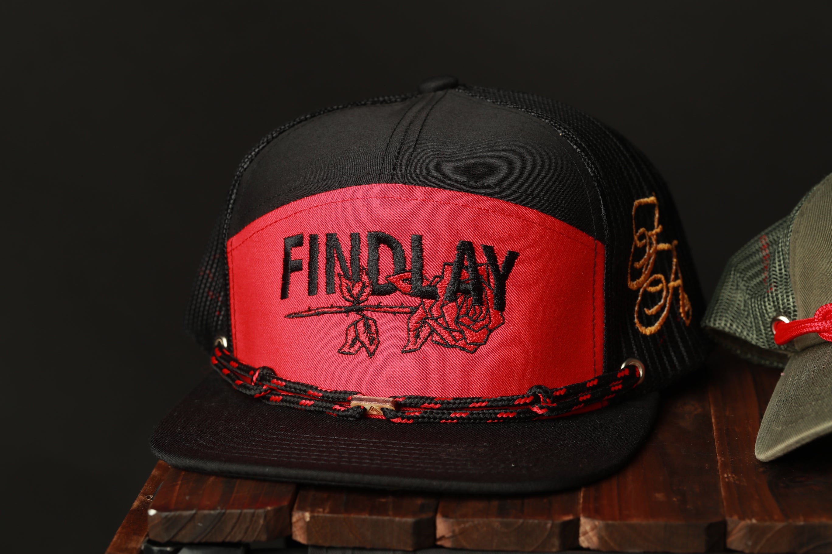 A black and red baseball cap with the word "FINDlay" printed on it, sitting on a wooden surface.