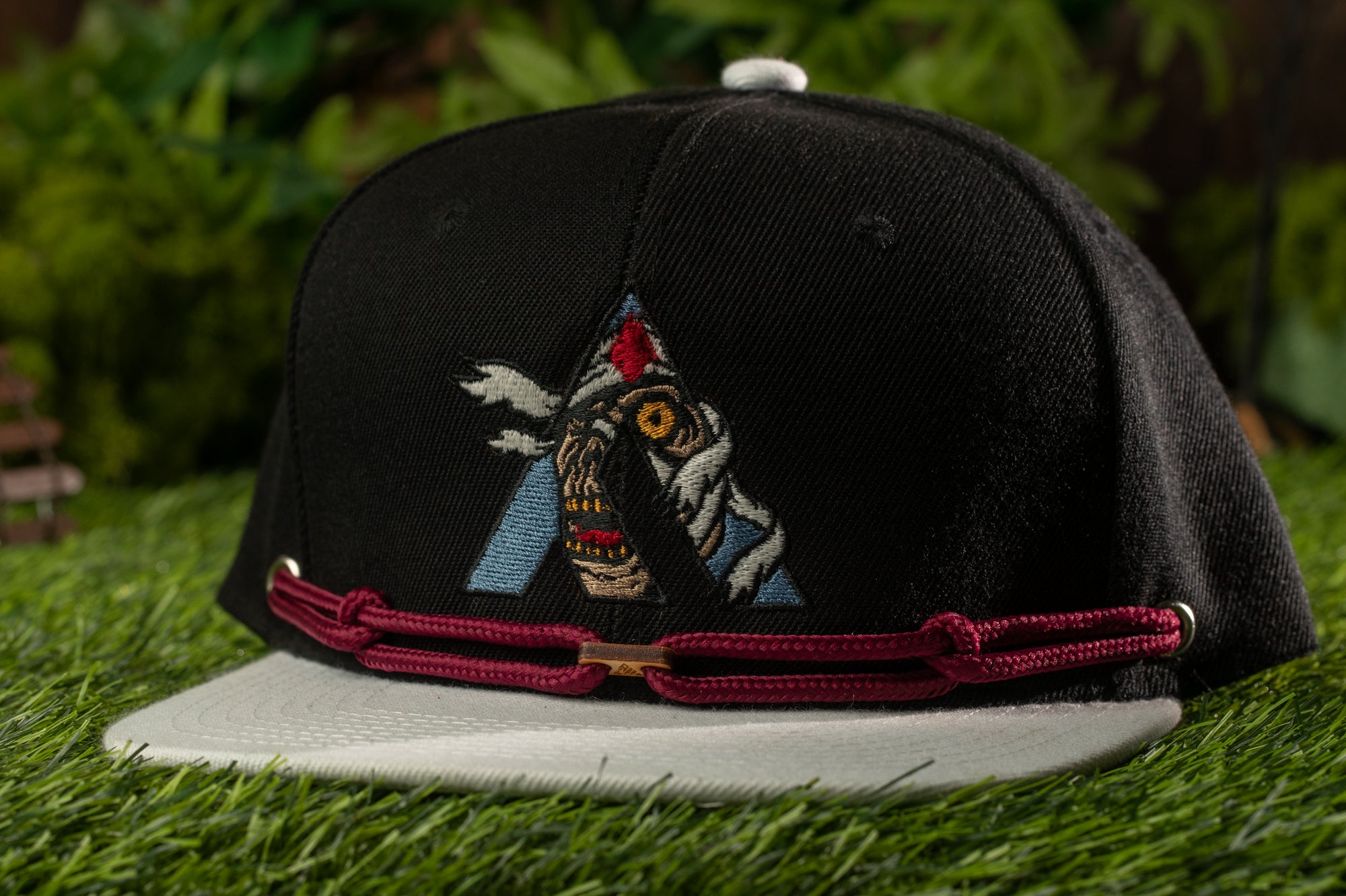 A black baseball cap with a colorful graphic design on the front, placed on a grassy surface.
